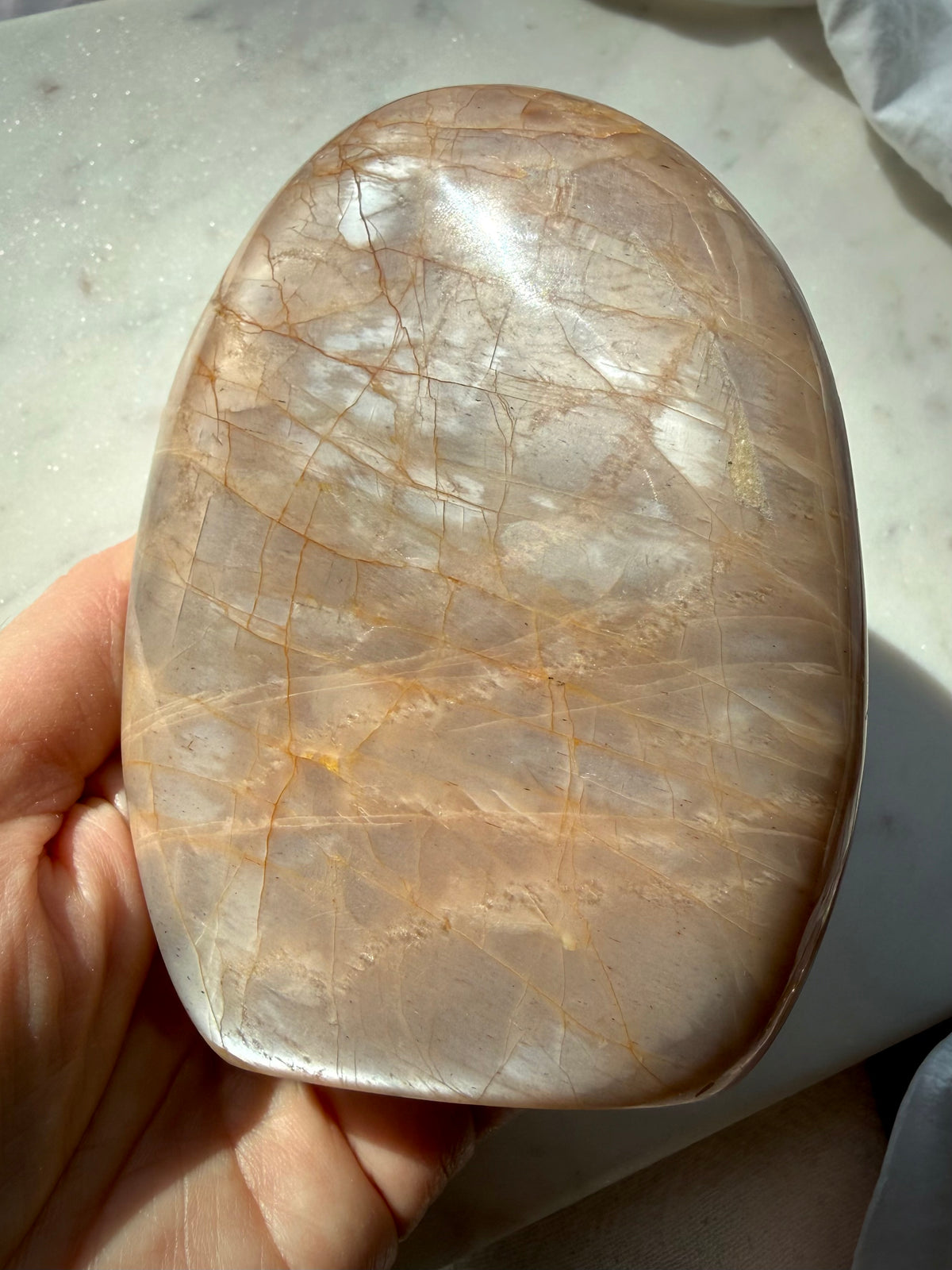 Polished Peach Moonstone crystal held in hand with luminous silvery sheen and natural peach color variations