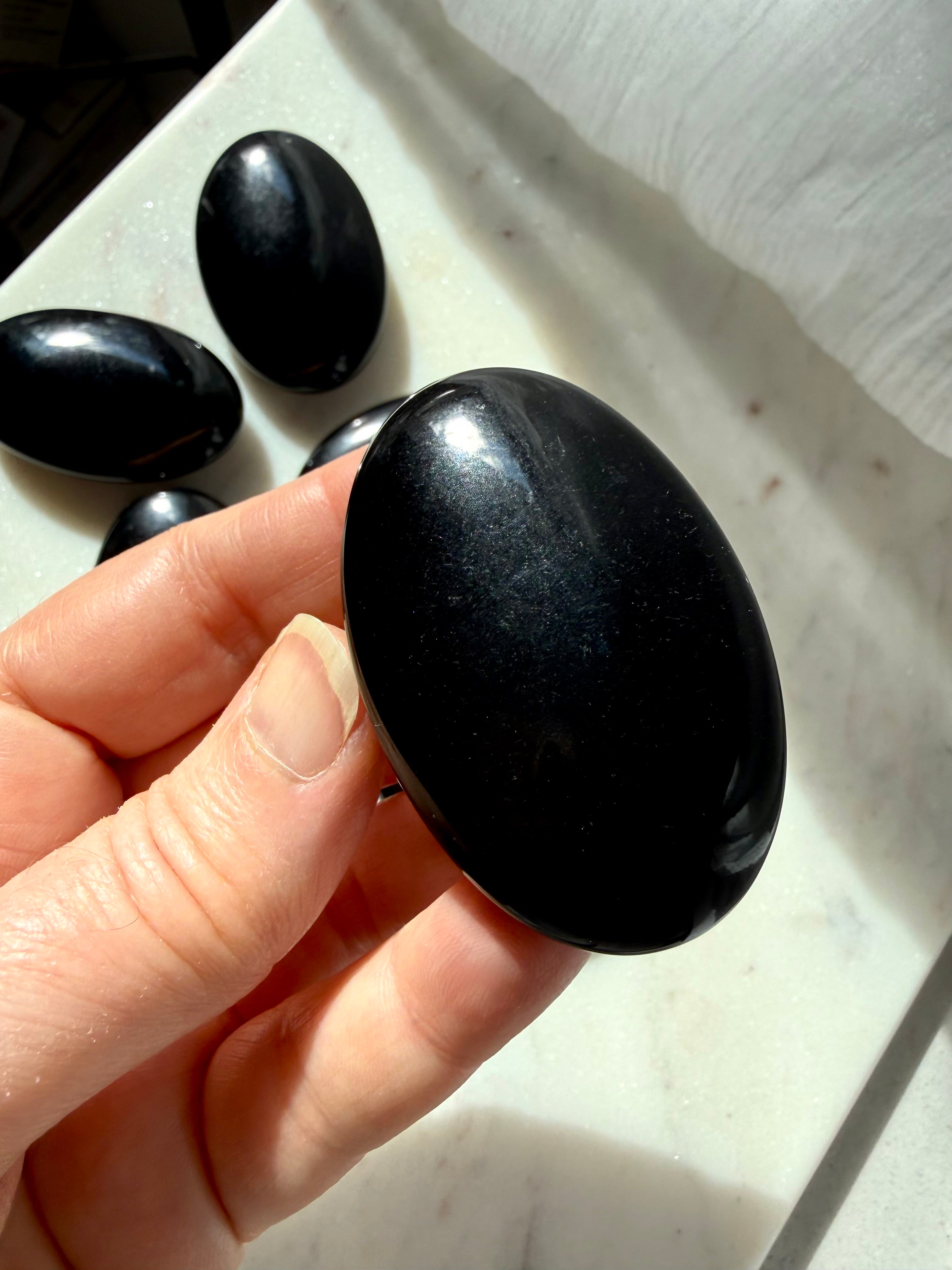 Polished Black Obsidian palm stone in hand with glossy mirror-like finish and comforting oval shape 