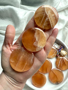 Hand holding three polished honey calcite discs with natural banding and warm golden tones for confidence, clarity, and gentle empowerment.