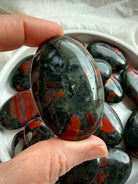 Bloodstone palm stone held in hand with deep green matrix, bright red inclusions and natural golden pyrite specks