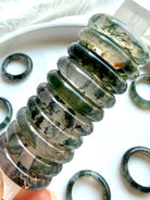 stacked moss agate band rings on selenite wand highlighting translucence and natural dendritic inclusions, crystal rings for grounding, clarity, and heart chakra balance