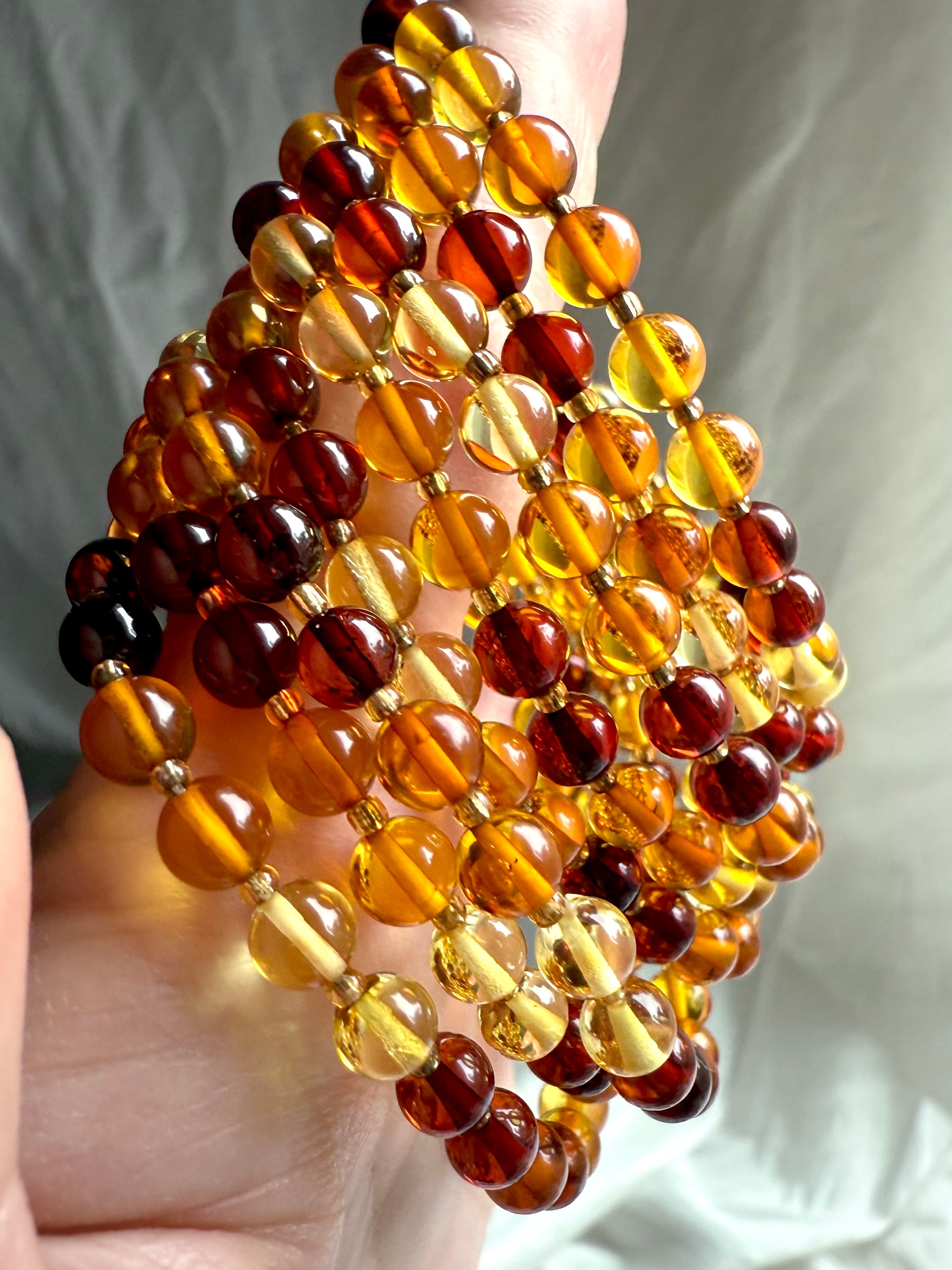 Amber bracelets draped in hand with vibrant color variation – energizing crystal jewelry for confidence + life force