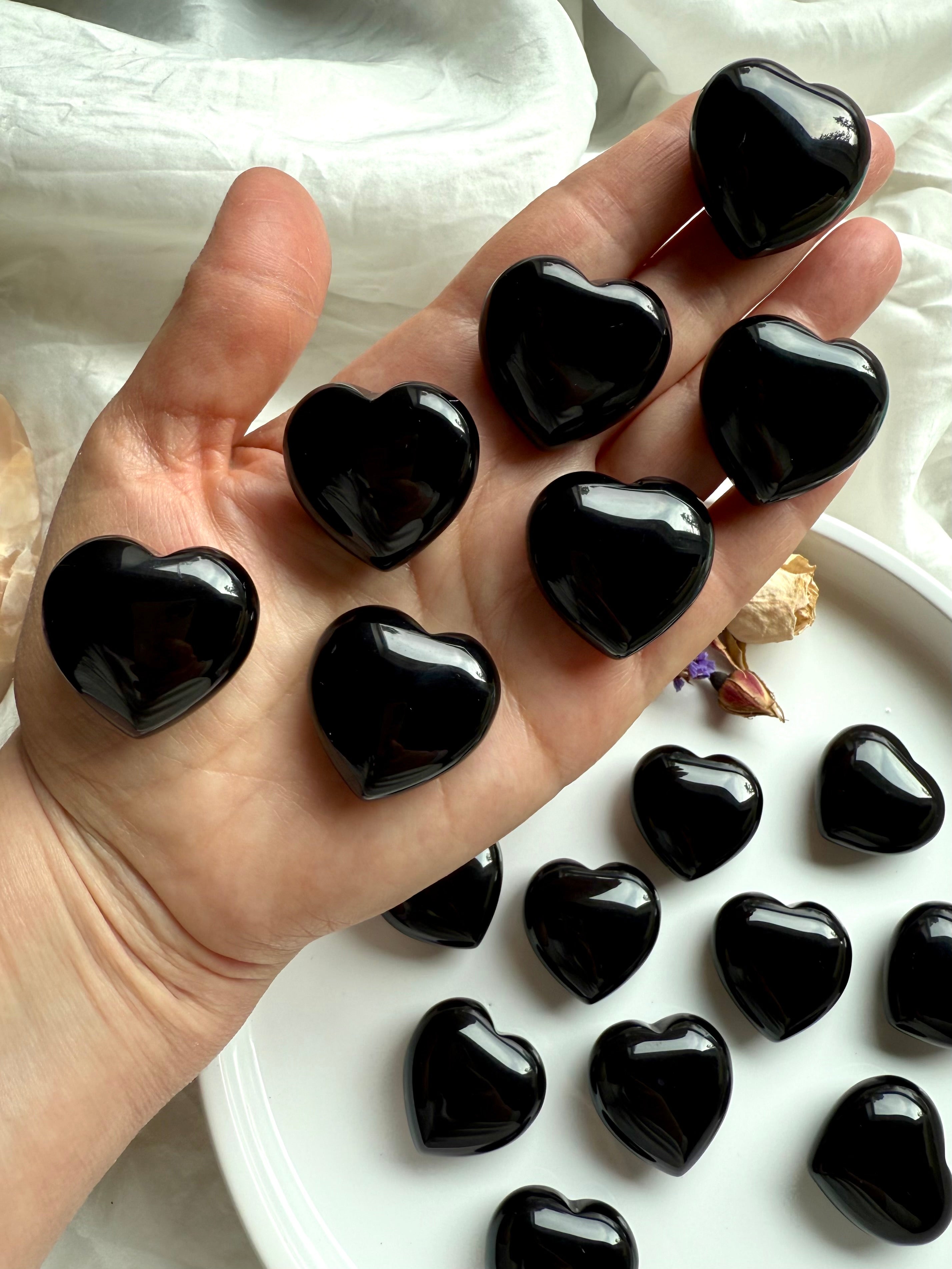 Palm filled with glossy Black Obsidian heart crystals, showcasing their size and shape.