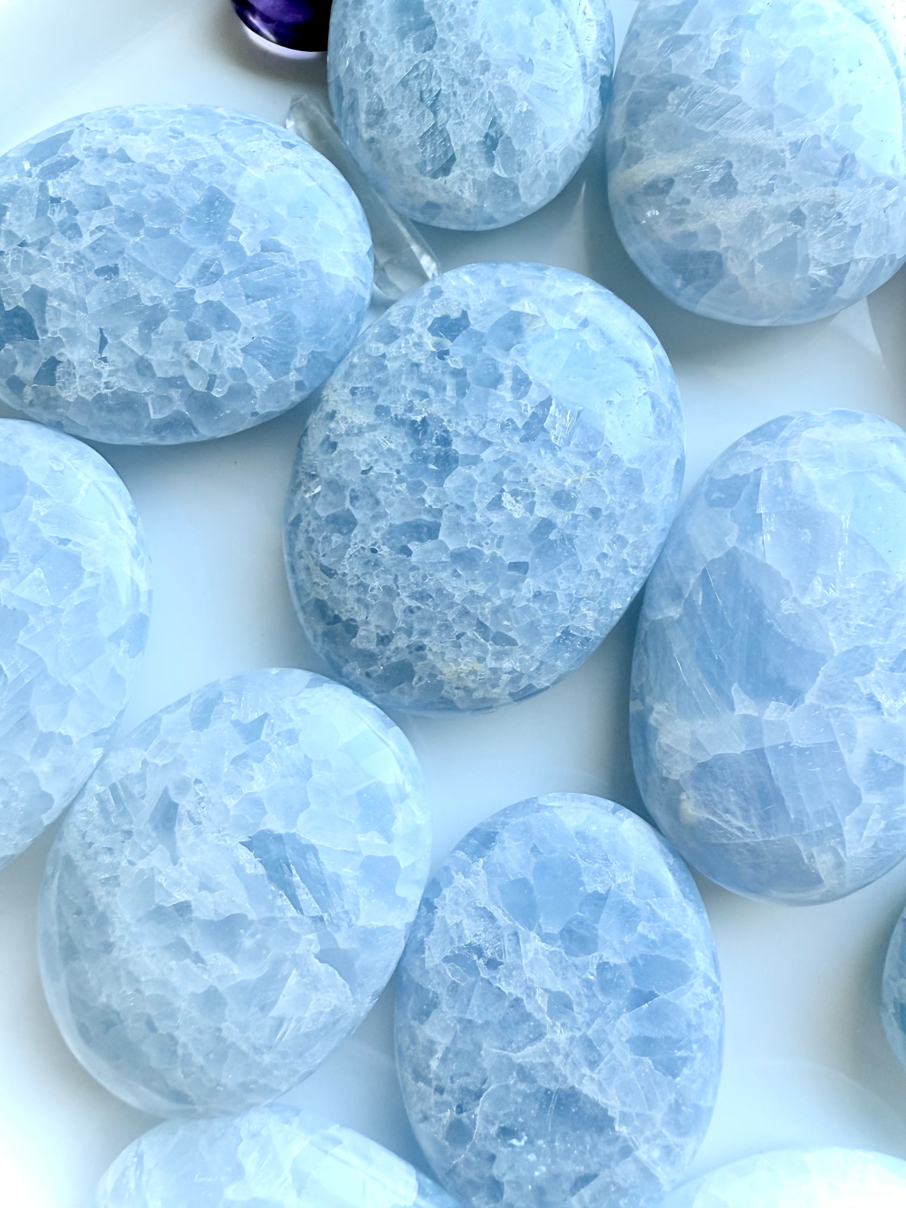 Array of Blue Calcite palm stones in soft pale blue hues, each with unique crystalline patterns and shapes