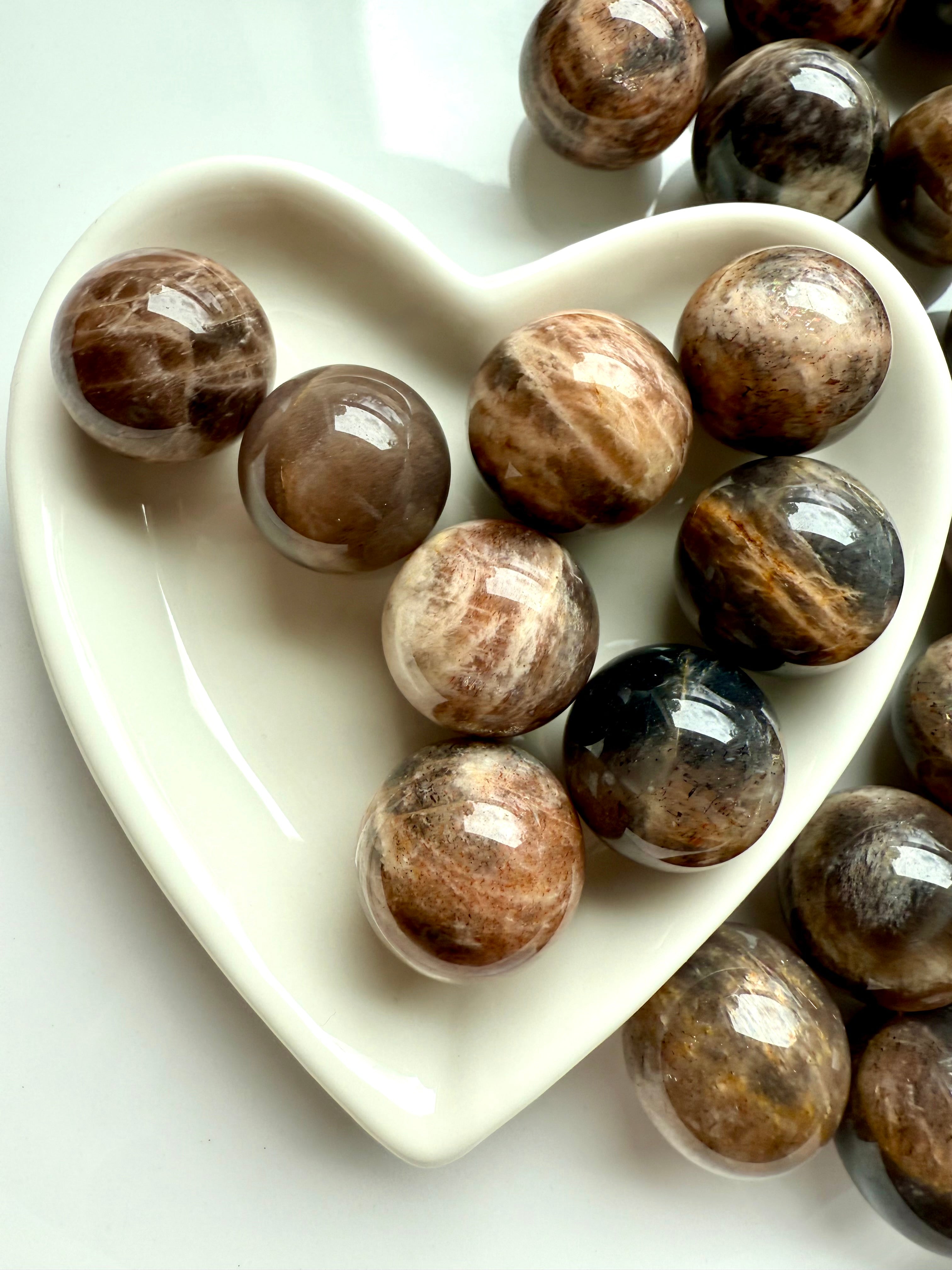Closeup of Mini Black Moonstone spheres with Sunstone shimmer displayed in a white heart-shaped bowl