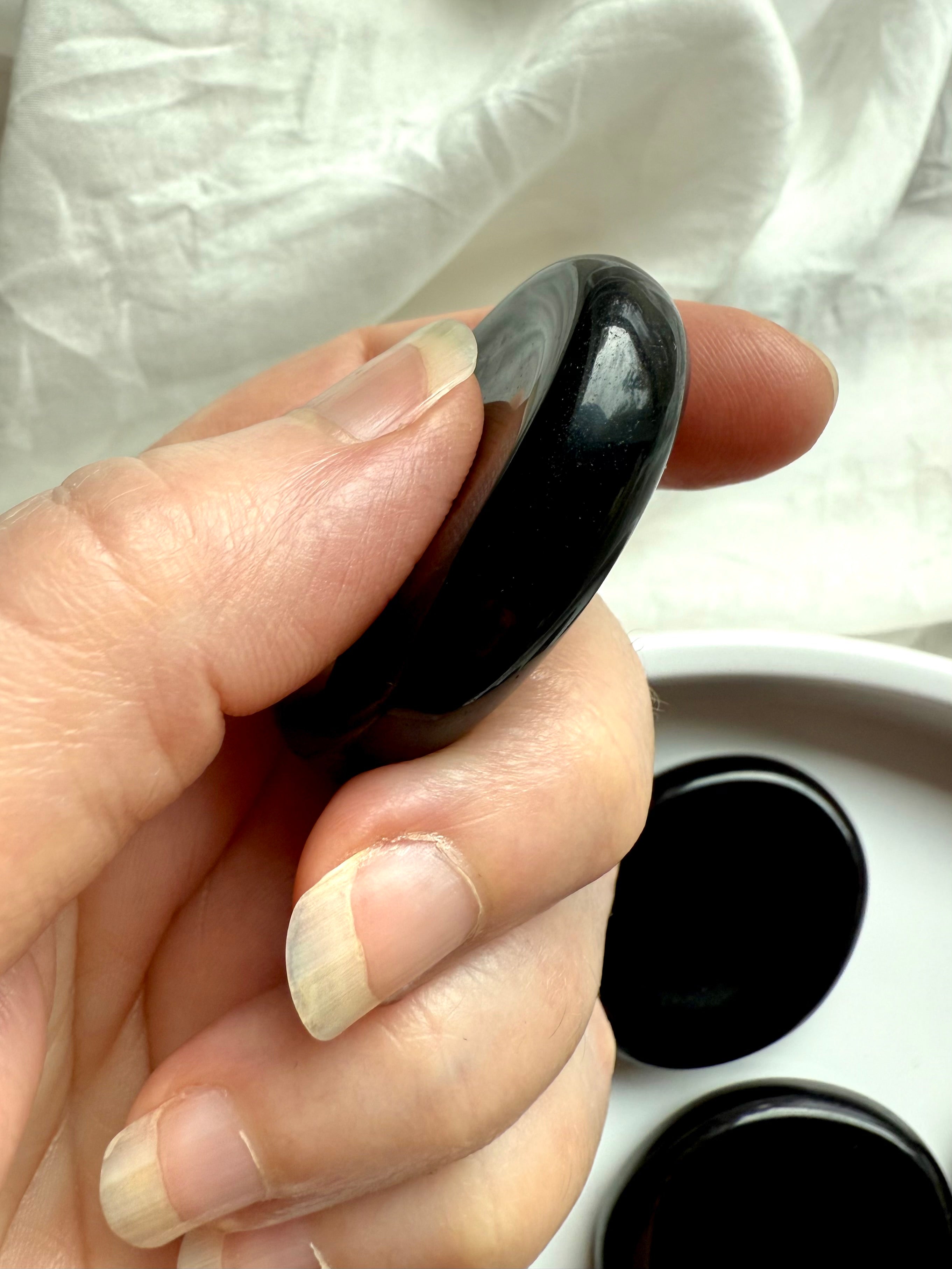 Black Obsidian worry stone in hand – thumb indentation for calming anxiety, grounding + meditation support