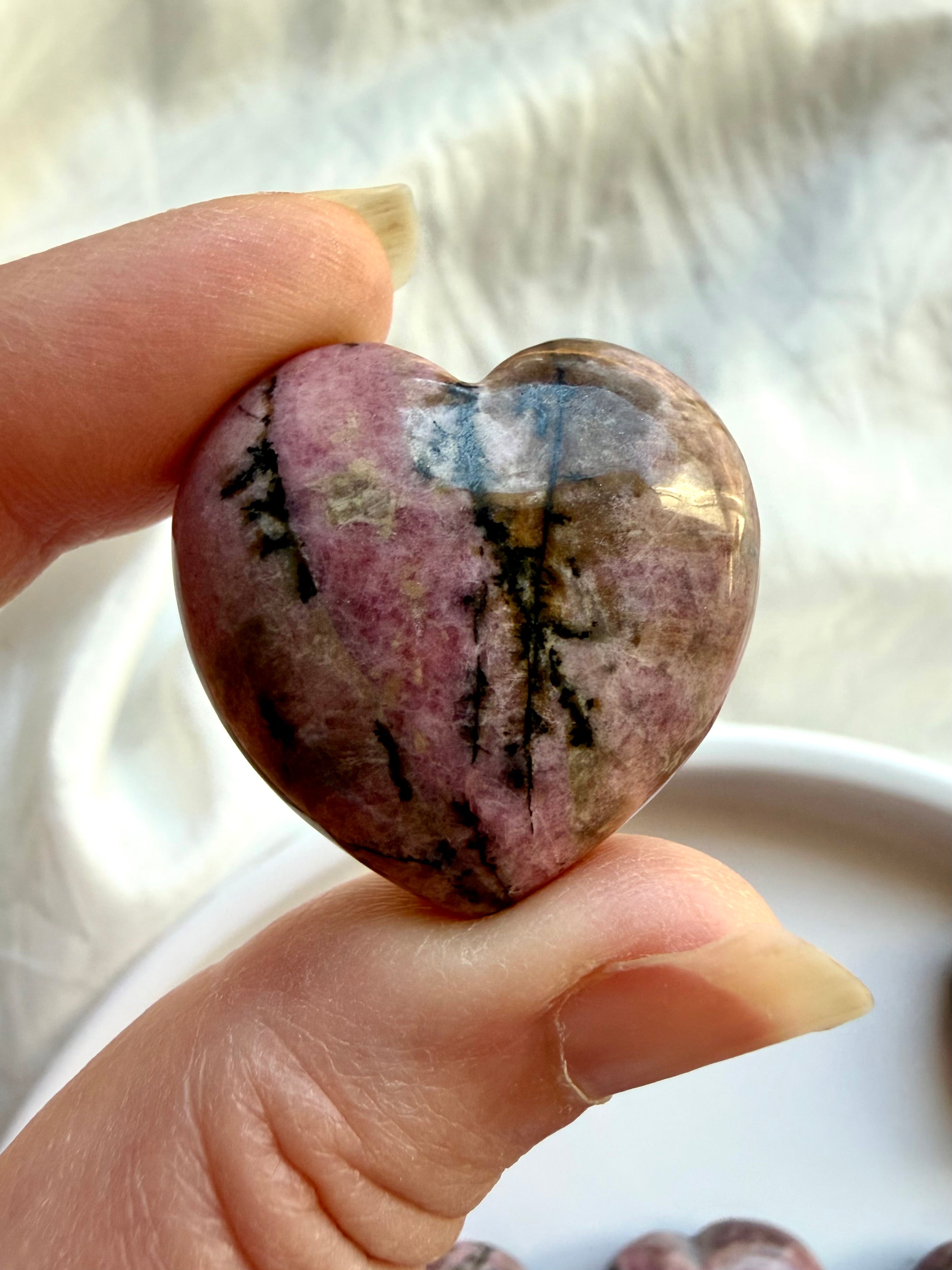 Rhodonite crystal heart held in hand showing natural pink color, dark veining and earthy mineral inclusions