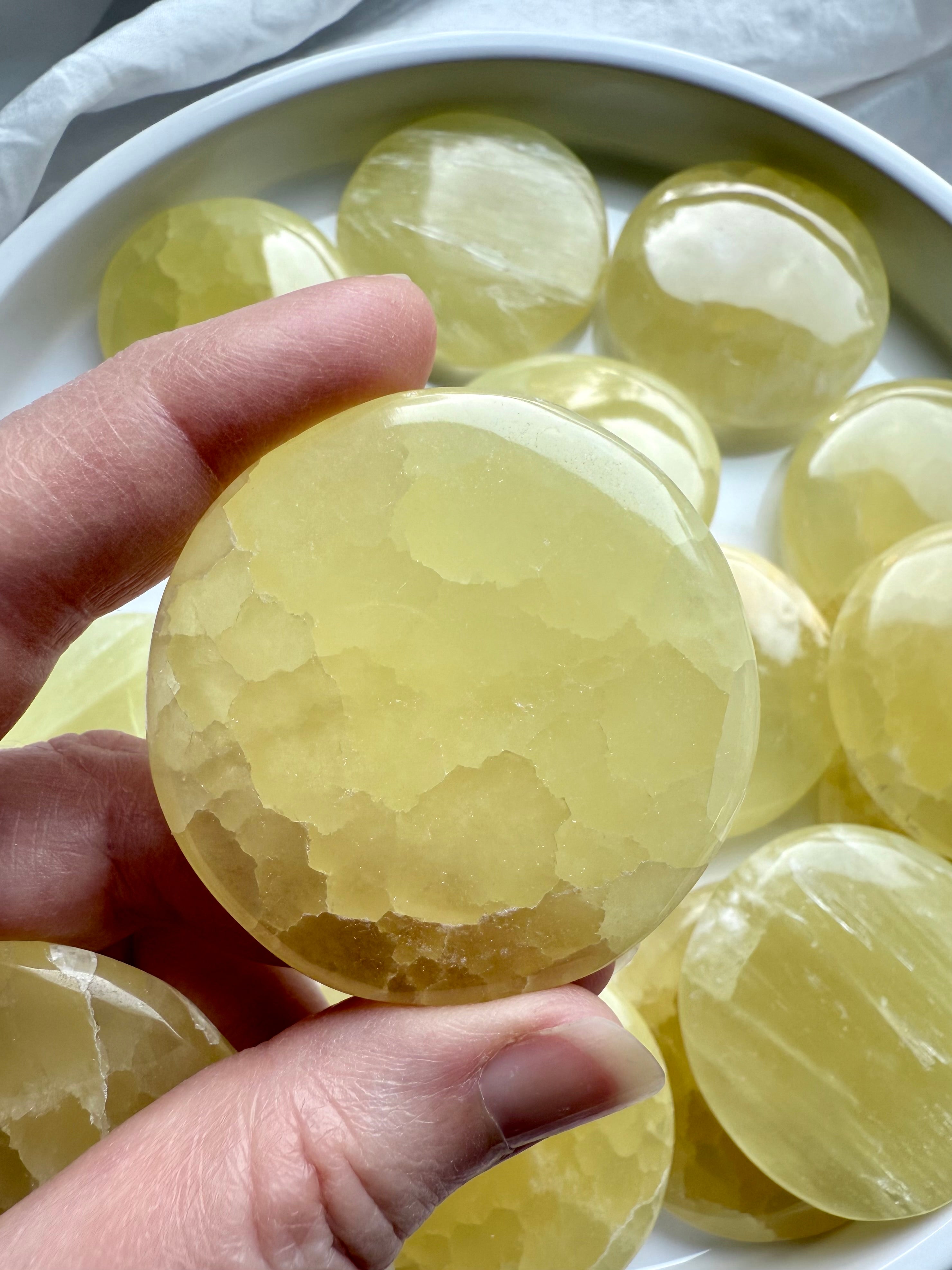 Polished lemon calcite meditation stone held above a white bowl filled with yellow crystals