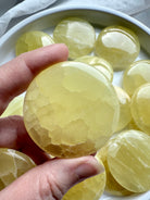 Polished lemon calcite meditation stone held above a white bowl filled with yellow crystals