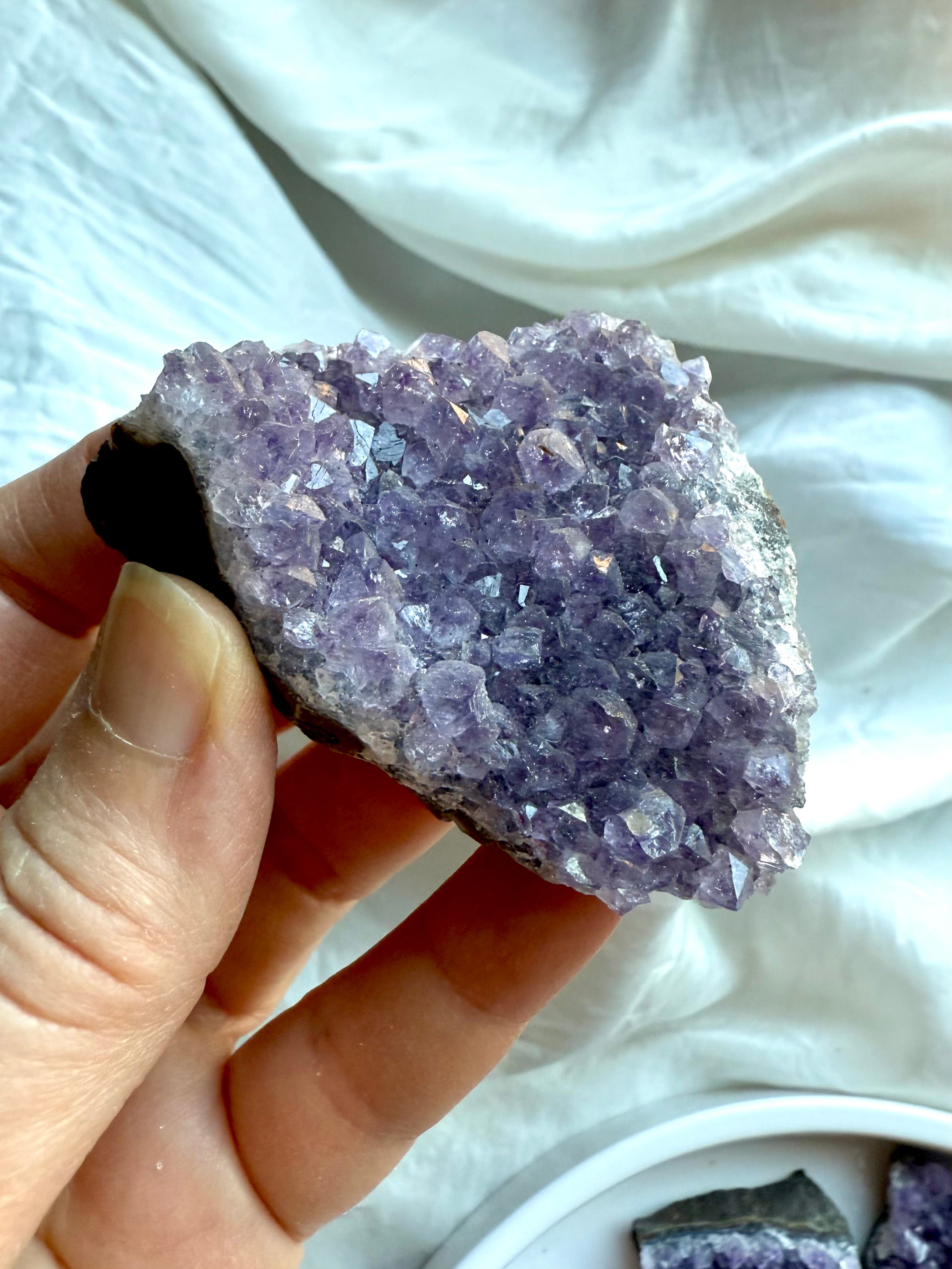Closeup of natural amethyst geode cluster held in hand over white silk. Third Eye Chakra crystal for intuition.