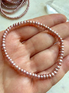 one pink freshwater pearl bracelet held in hand, close-up of small round pearls with natural luster and soft pink tones