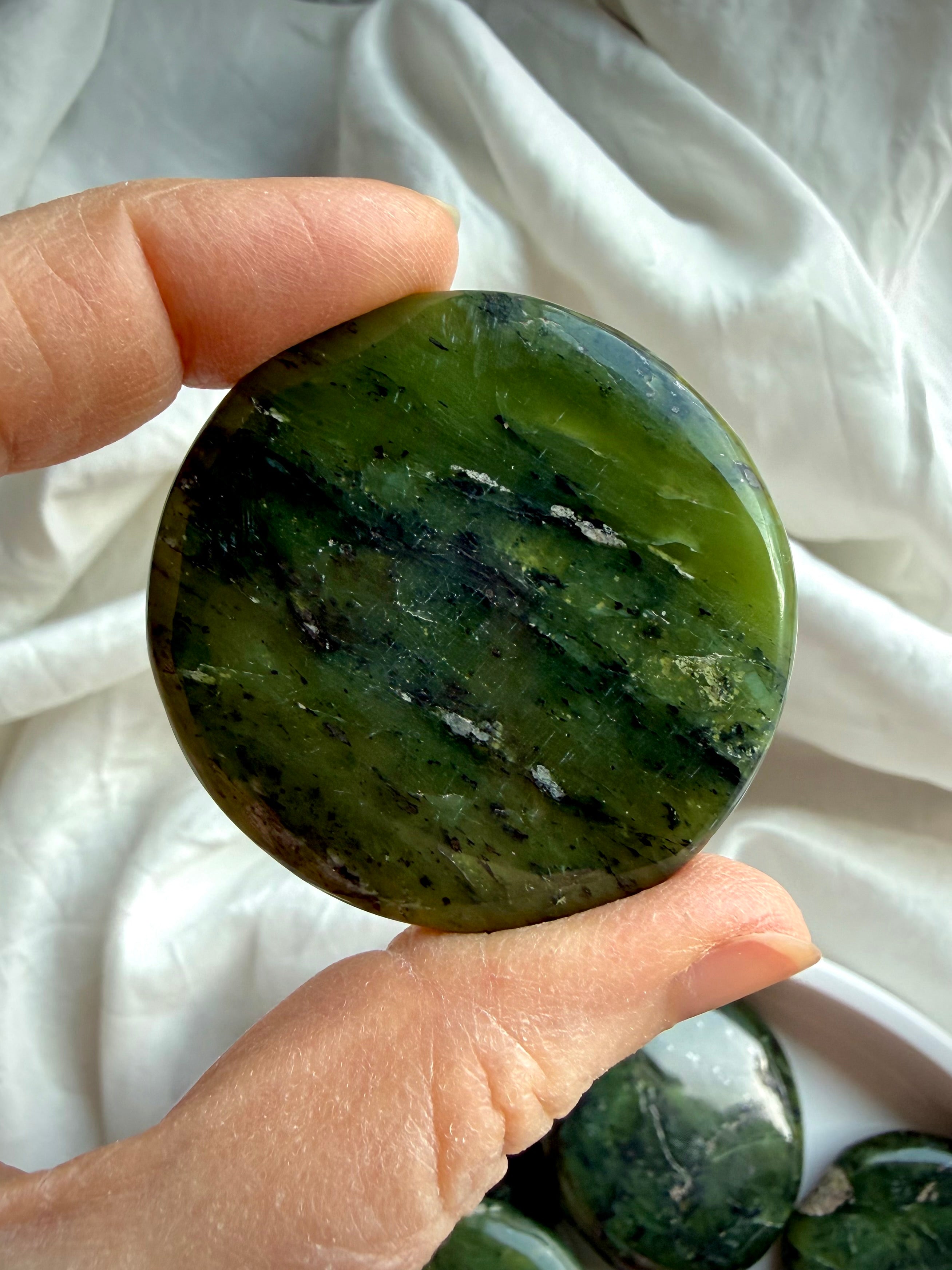 Nephrite jade palm stone held in hand showing deep forest green marbling and natural veining, grounding crystal for heart chakra healing