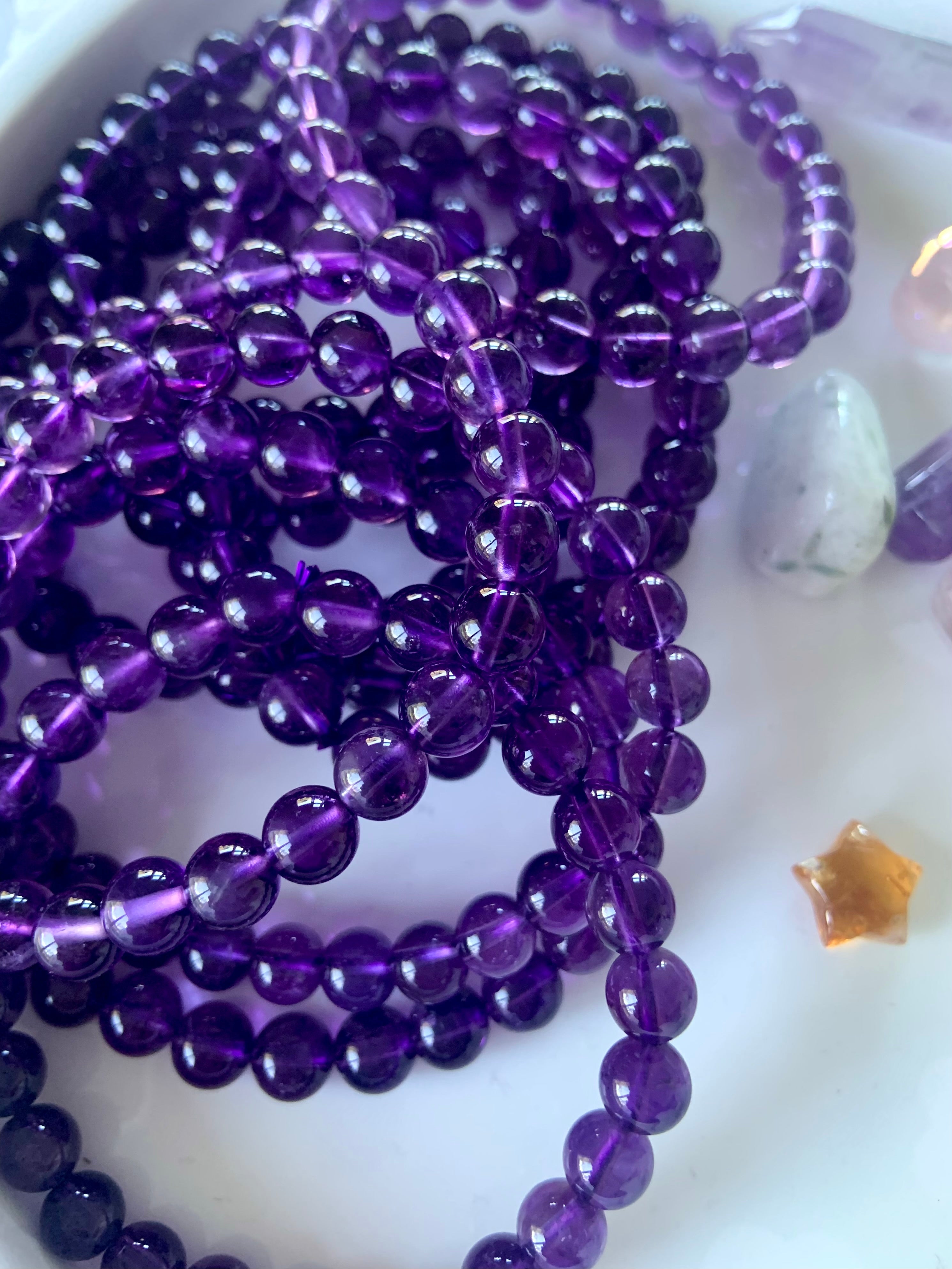 An array of high quality amethyst bracelets on a white plate with other mini crystals in the background