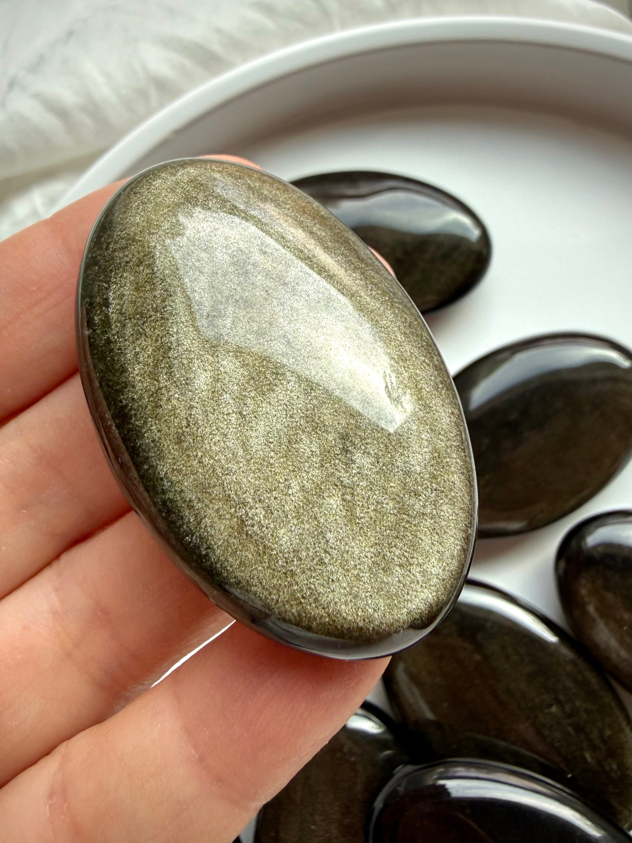 Golden Sheen Obsidian palm stone held in hand with radiant gold shimmer for protection, personal power and meditation