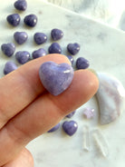 Tiny Lilac Lepidolite heart crystal balancing on a fingertip showing the puffy heart shape