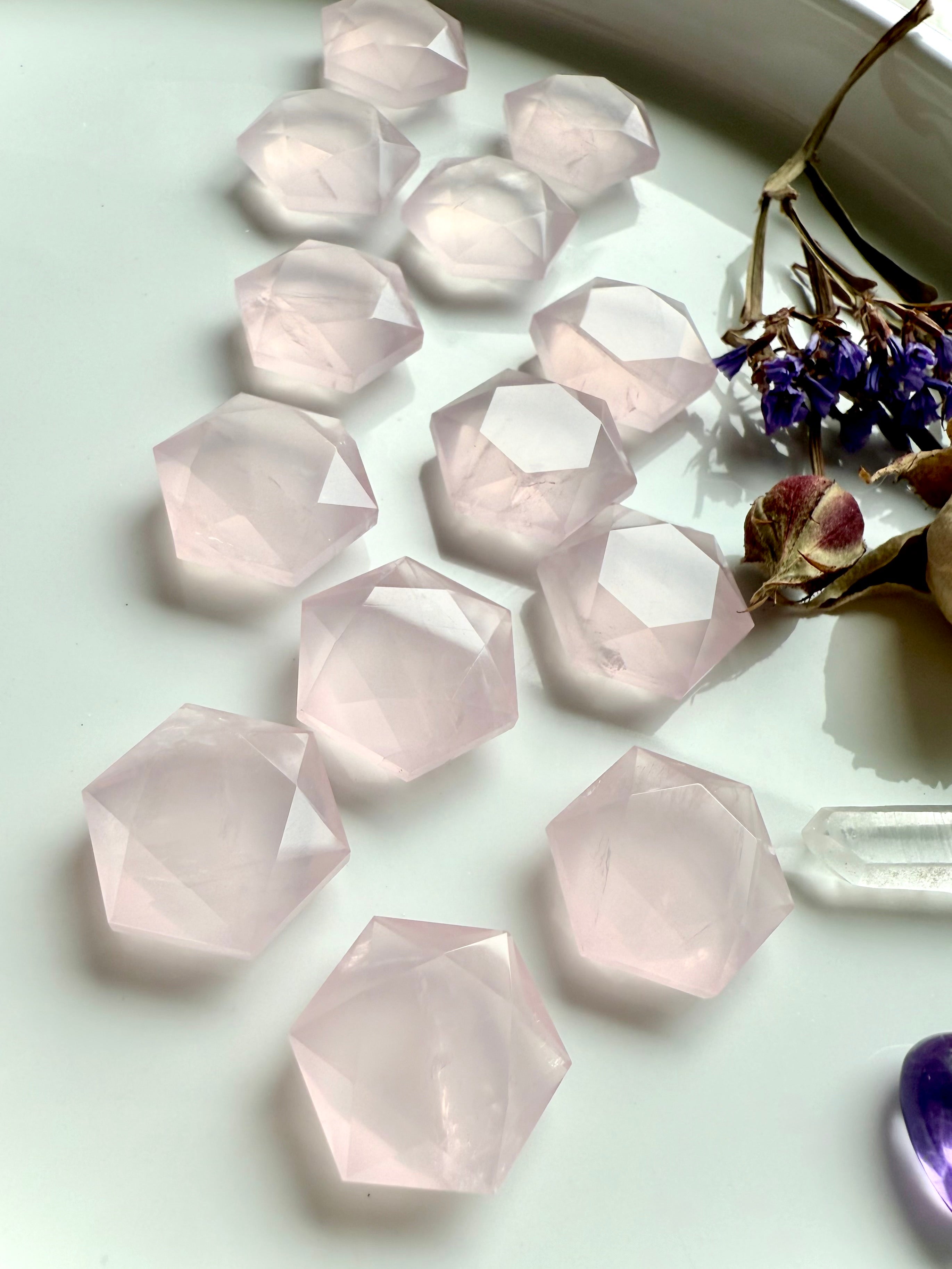 Closeup angled array of mini rose quartz hexagon crystals on white background, translucent pink sacred geometry carvings for Heart Chakra healing