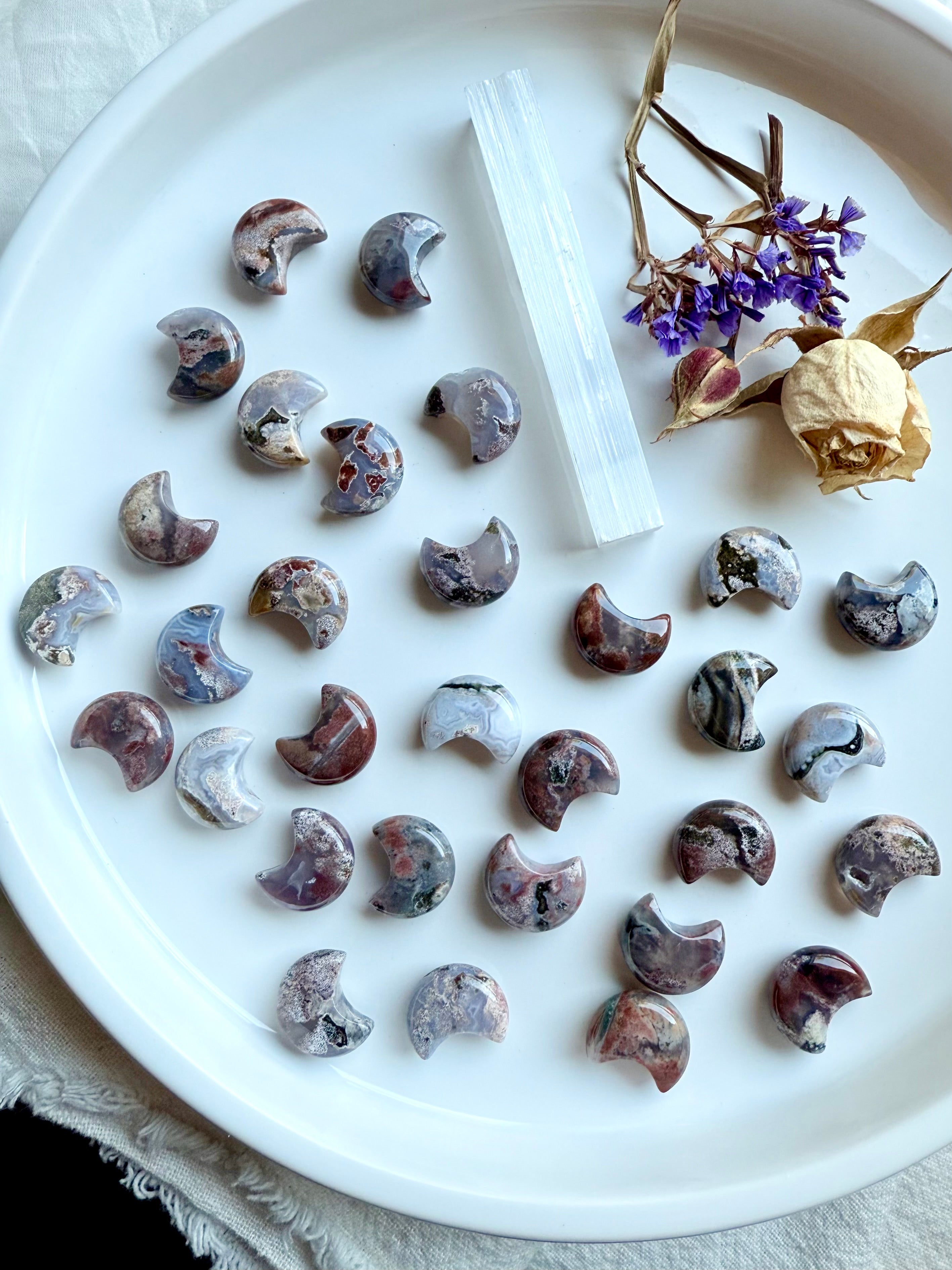 Ocean Jasper crescent moon carvings on white dish with selenite wand and dried flowers, celestial crystal carvings for altar décor and crystal grids