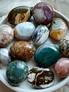 Ocean Jasper palm stones, also known as Sea Jasper, in a white bowl showcasing teal, pink, cream, green, and brown colors with orbicular patterns