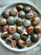 Mini Polychrome Jasper crystals in a white bowl, showing a variety of polished rounded shapes and natural landscape-like formations