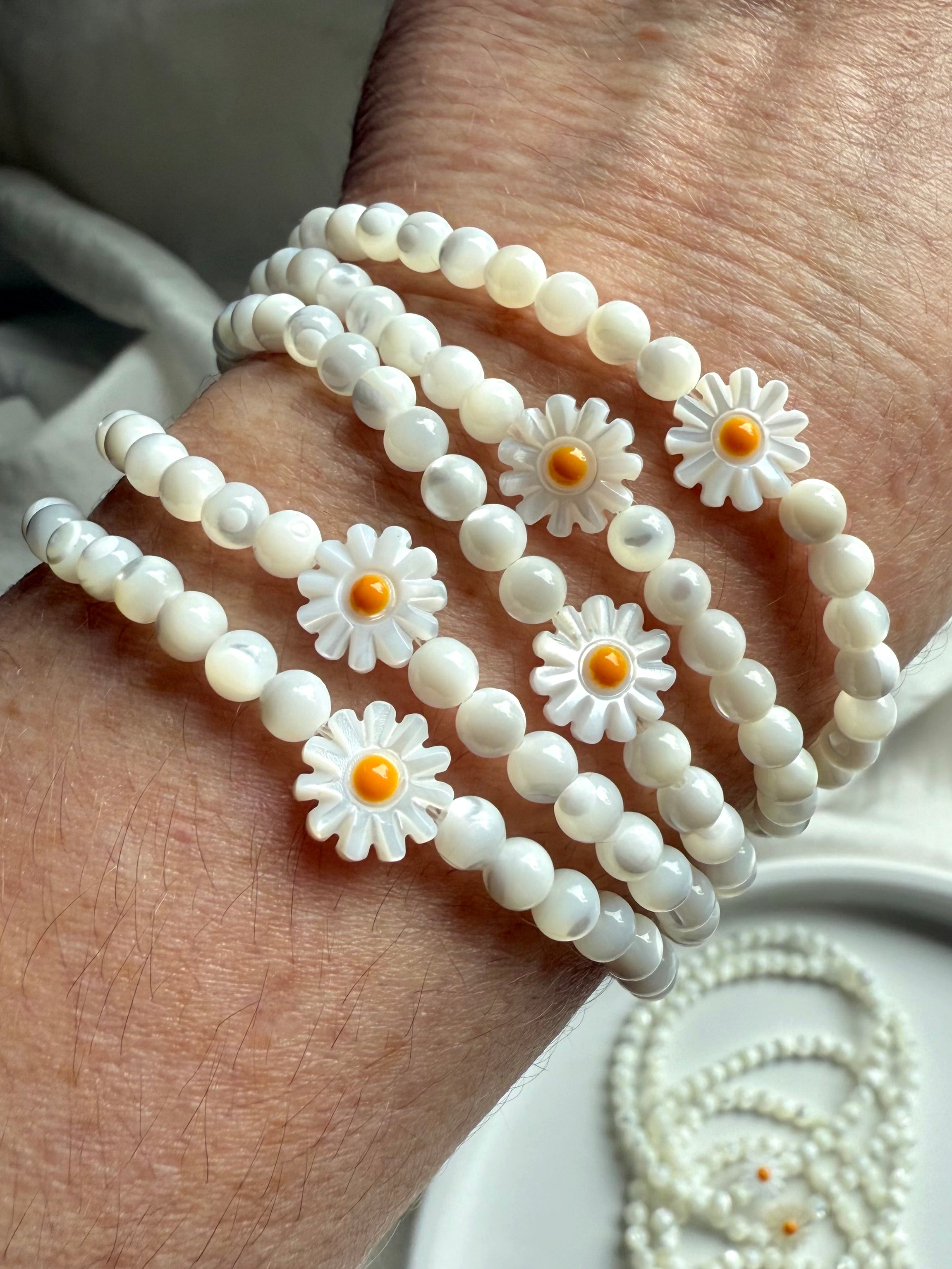 Multiple Mother of Pearl daisy bracelets stacked on wrist, glowing with soft iridescent shine – cheerful crystal jewelry gift