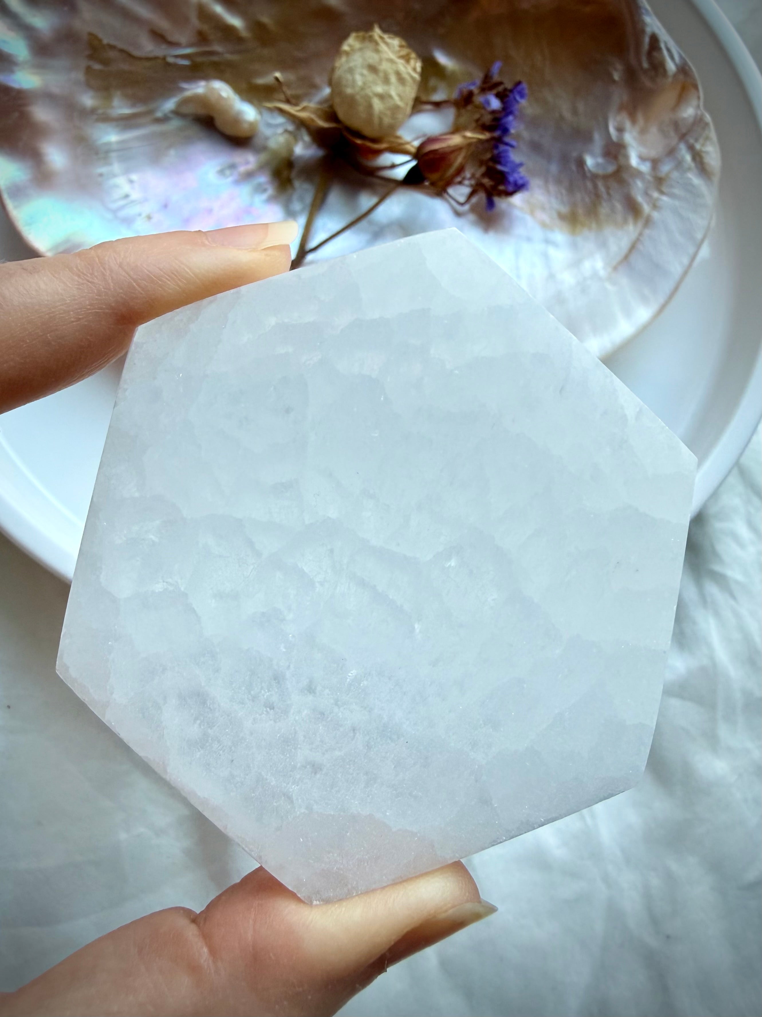 Selenite hexagon crystal plate held in hand showing natural white banding, a sacred geometry tool for cleansing and charging crystals