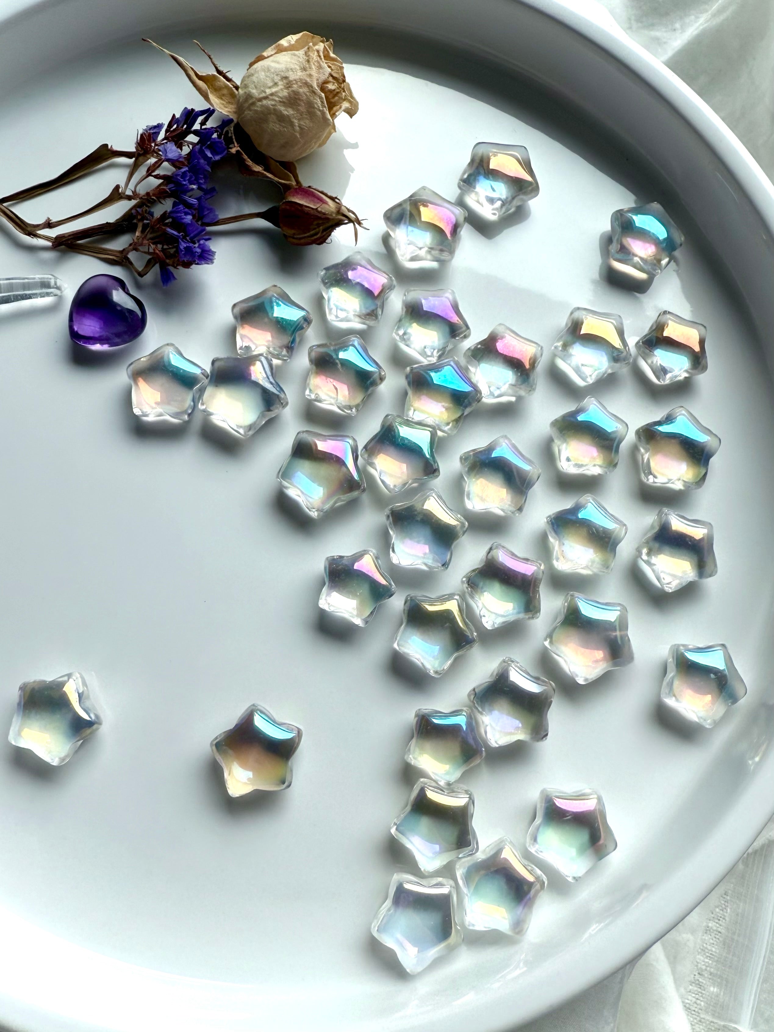 Opalescent mini aura quartz stars with rainbow sheen displayed on white tray with dried flowers, amethyst heart, and quartz points — healing crystals for universal chakra balance