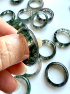 close-up moss agate ring between fingers with detailed dendritic patterning, translucent crystal for grounding clarity and renewal