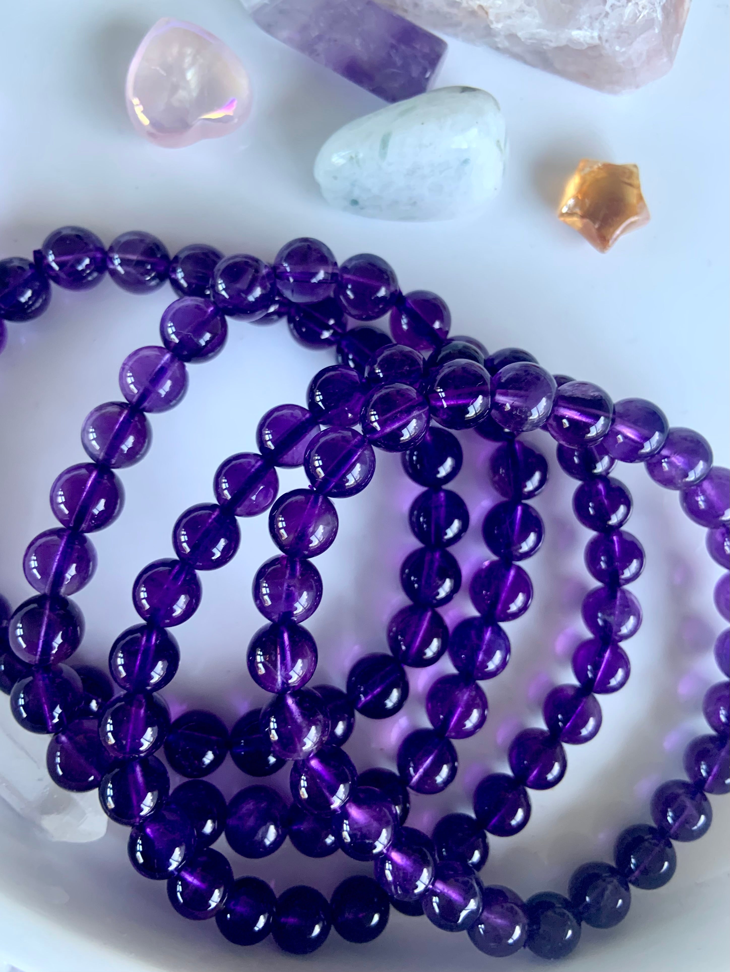 Overhead view of high quality deep purple amethyst beaded bracelets on a white plate with mini crystals in the background