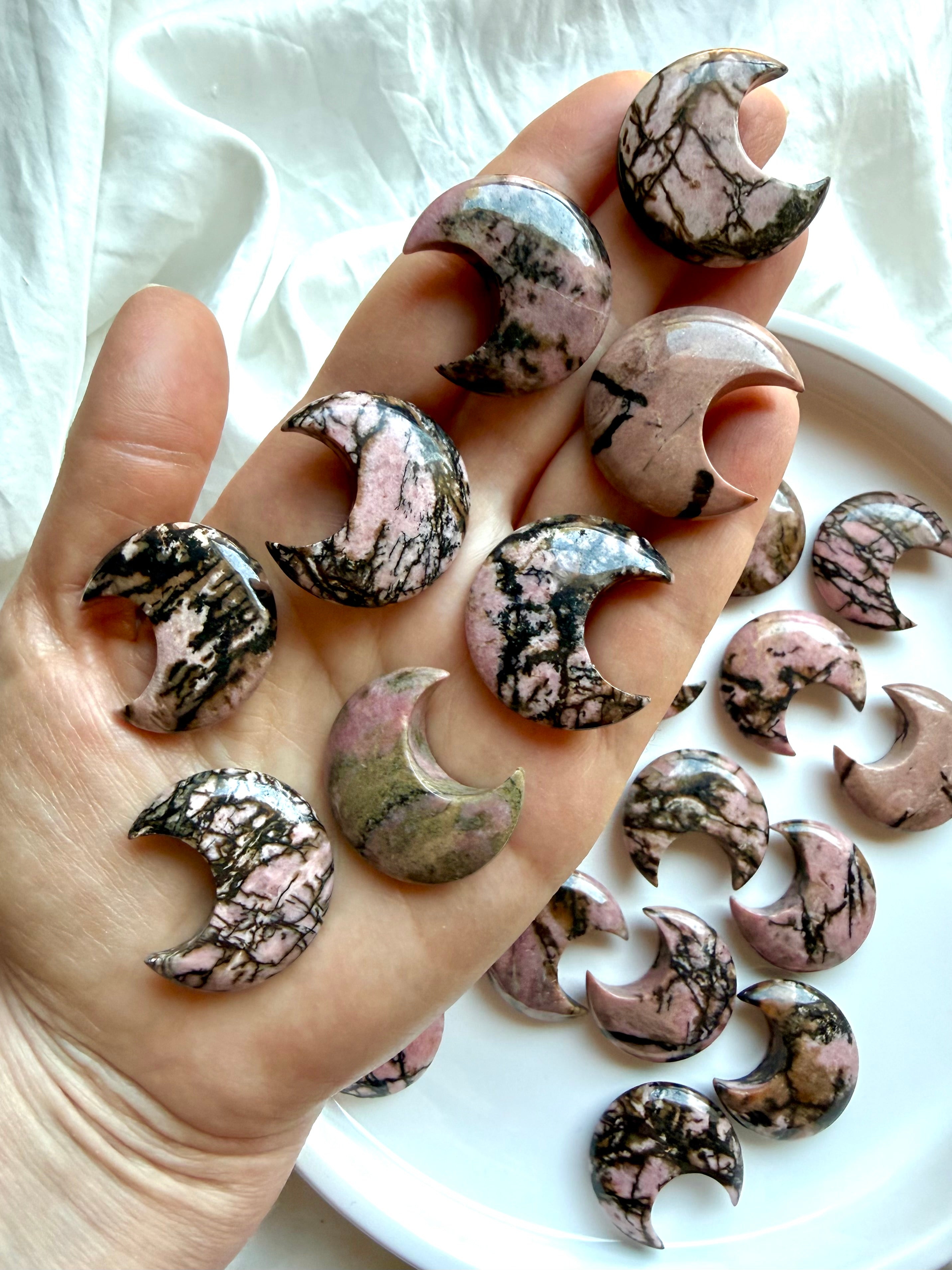 Rhodonite crescent moon crystals shown on hand showing natural color variations and polished finish for size reference