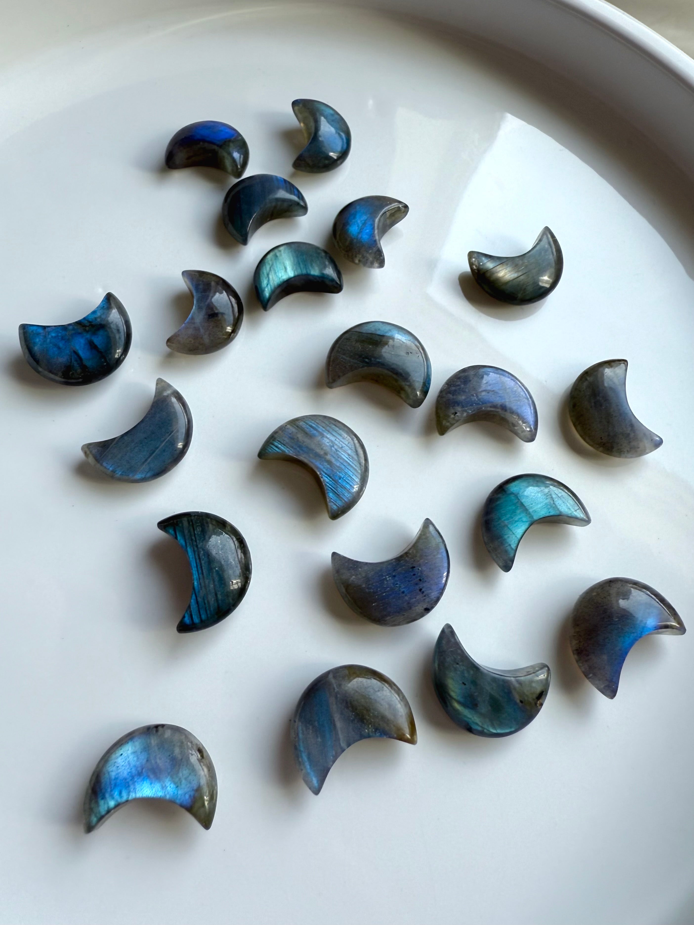 Wide angle overhead of mini Labradorite moons on a white plate — shimmering moon carvings for crystal healing, display & energy alignment.