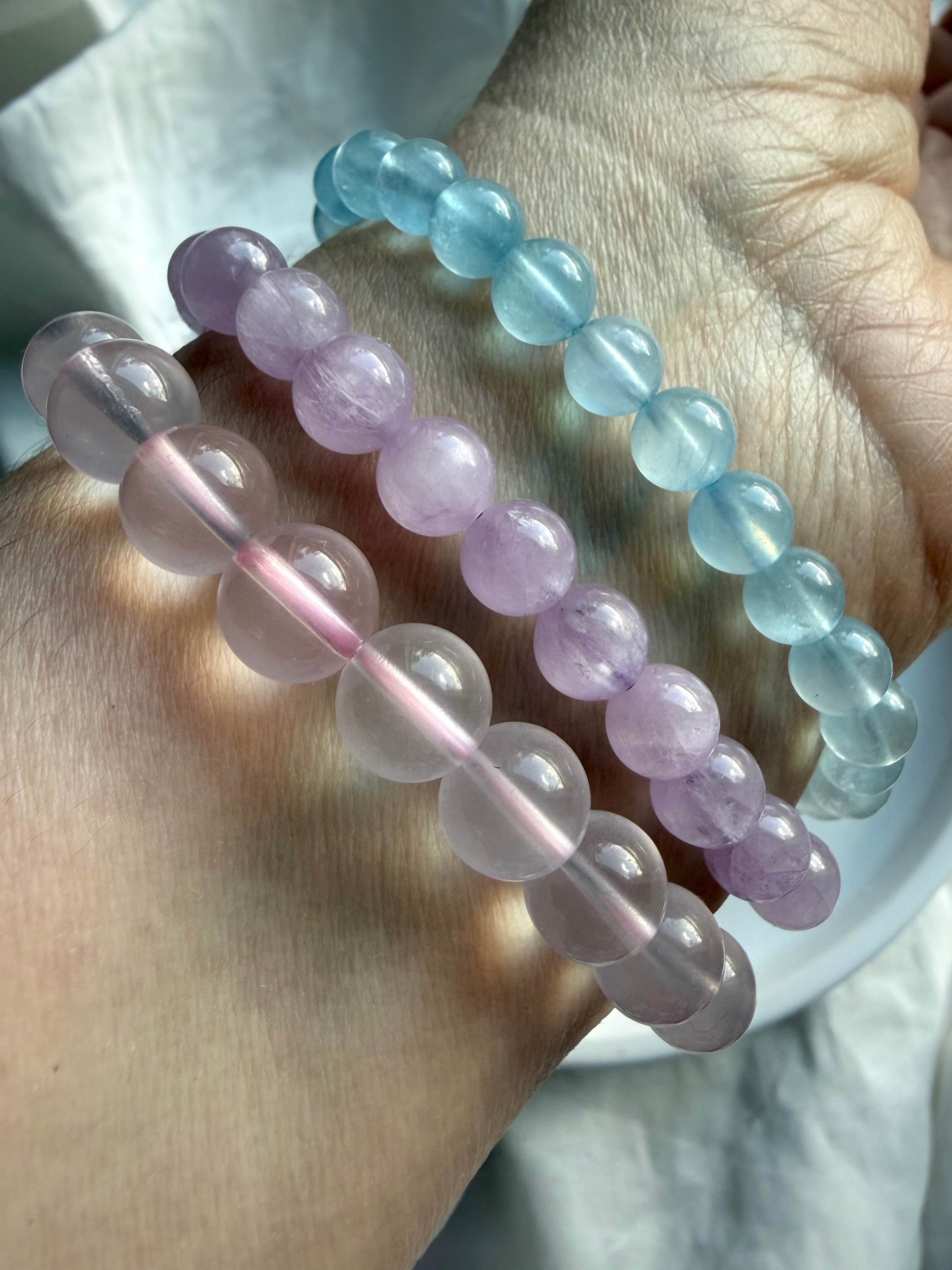 Stacked crystal bead bracelets on wrist featuring Aquamarine, lilac Kunzite and Mozambique Rose Quartz gemstone jewelry