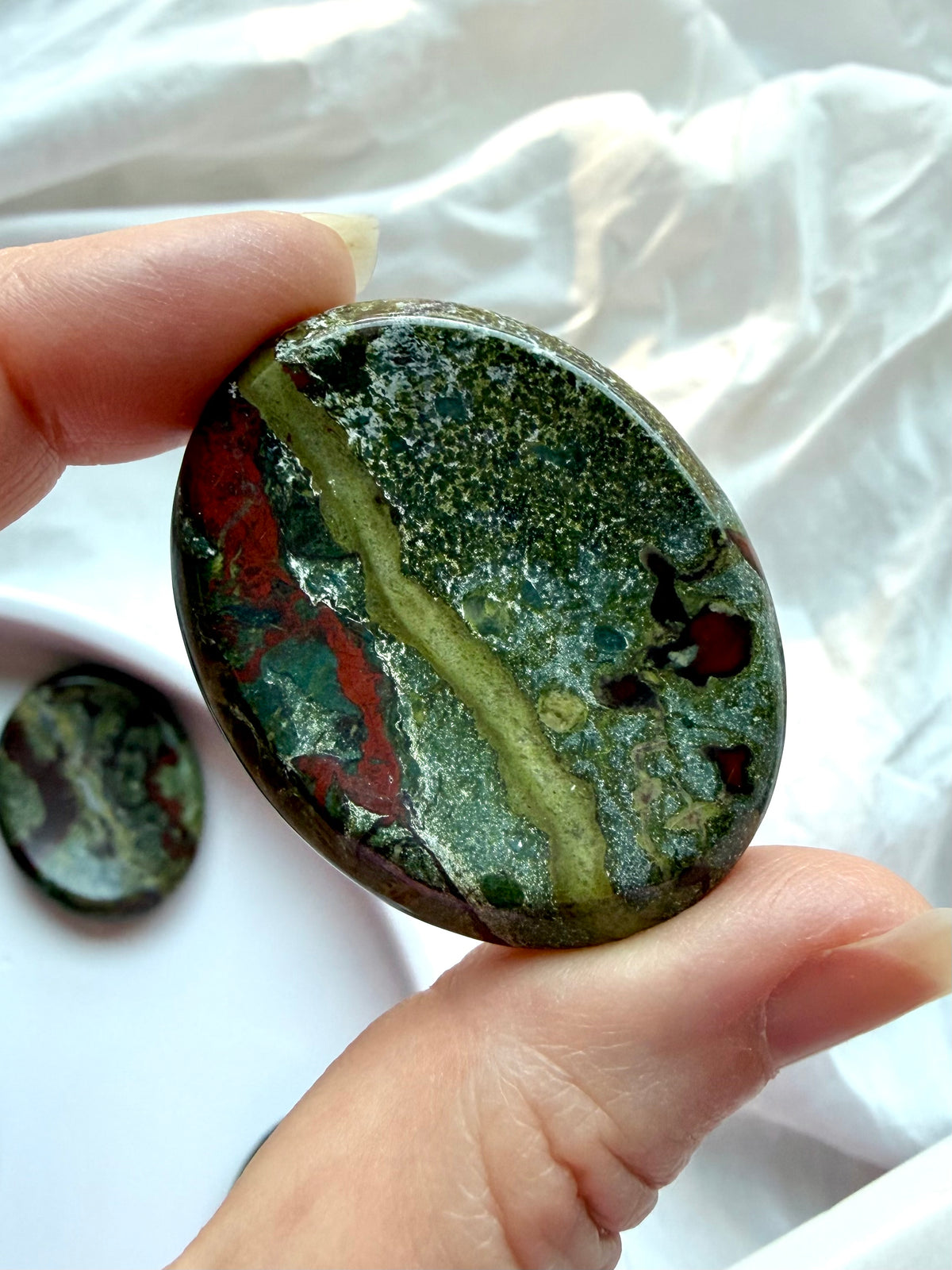 Oval Dragon Blood Stone worry stone held in hand, featuring deep green Epidote and flowing red Piemontite veins