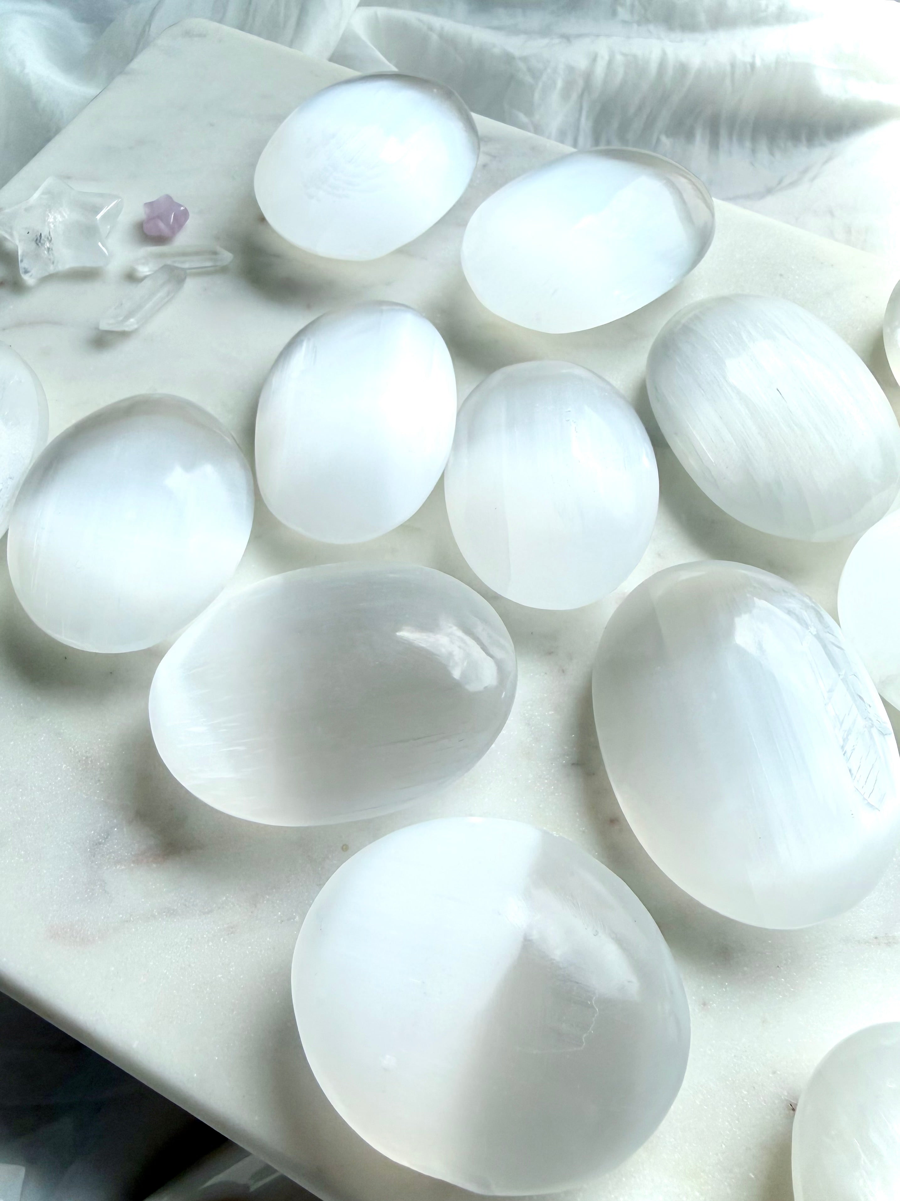 Collection of polished Selenite palm stones displaying luminous satin-like glow, natural variation, and glossy finish