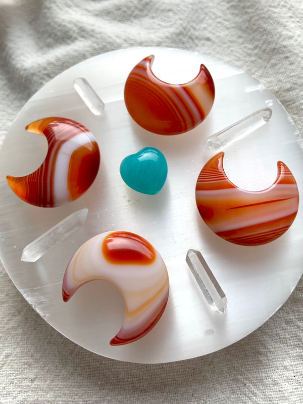 A crystal grid made from Banded Carnelian Moons, clear quartz points and an amazonite heart in the center on top of a selenite plate