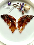 Carved Fire Quartz butterfly wings laid flat with dried flowers and clear quartz points for scale.