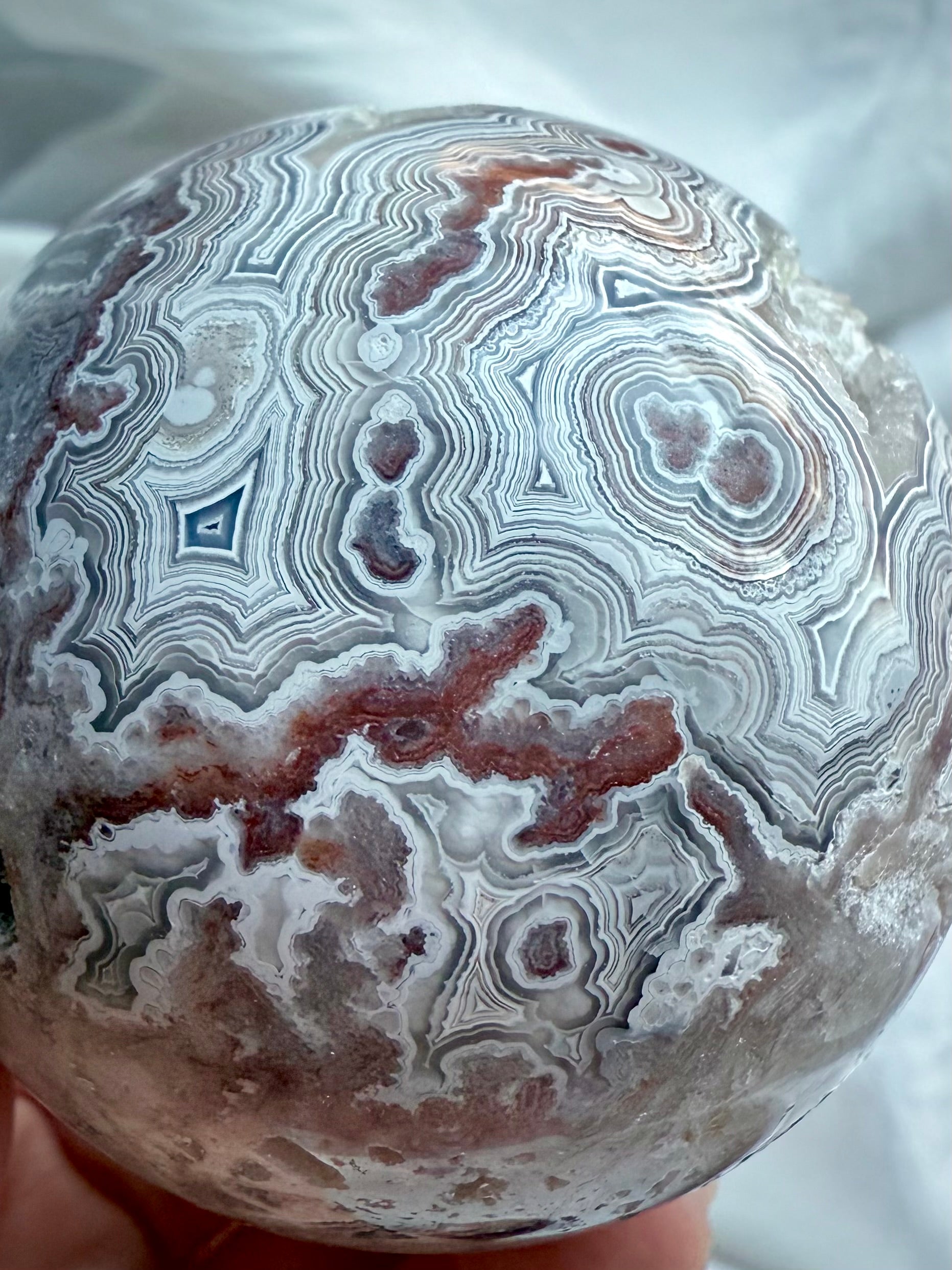 Close-up of high-grade Crazy Lace Agate sphere featuring geometric lace banding, crystal druzy pocket, and rich red tones