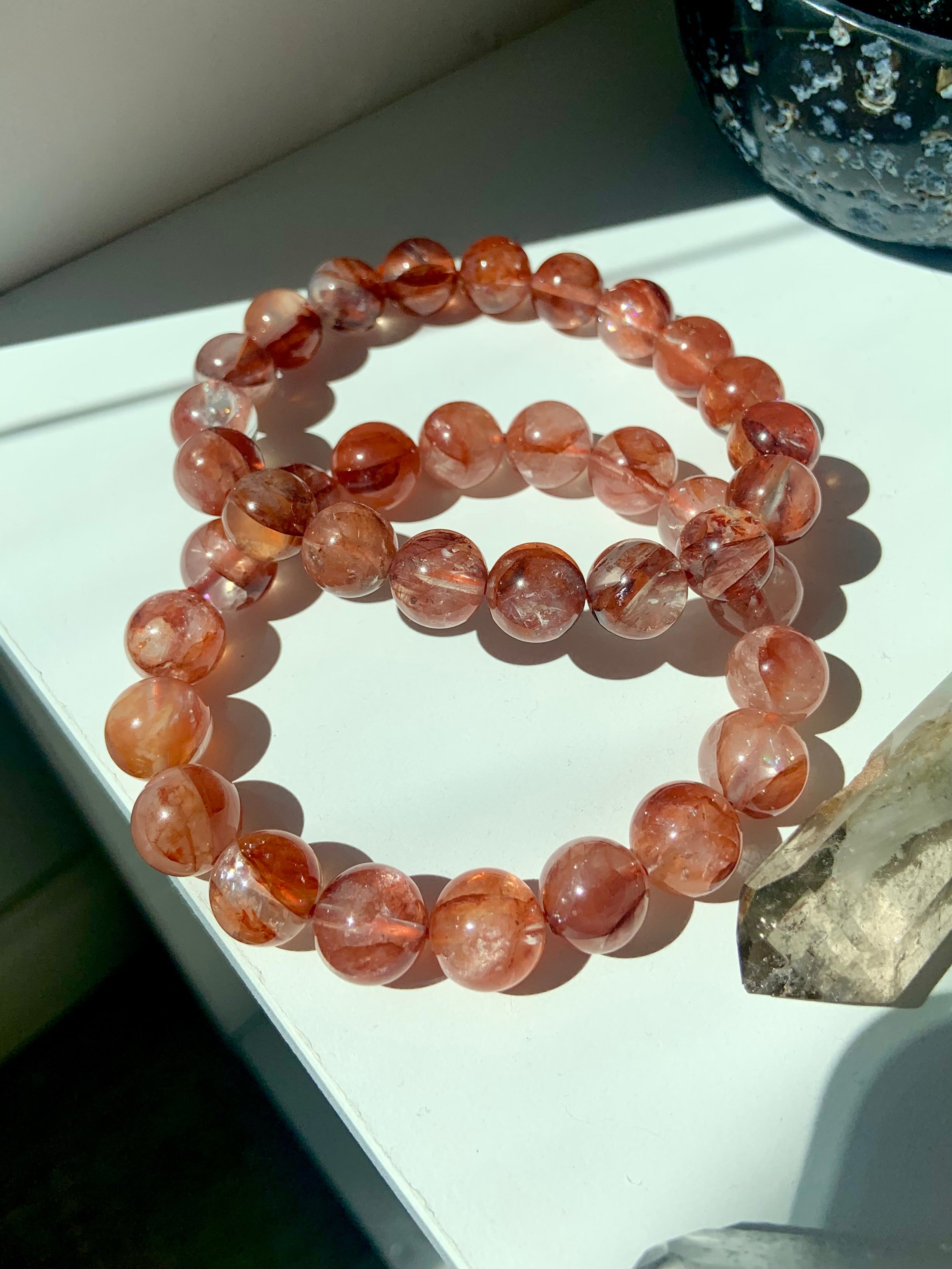 Lifestyle image of two Fire Quartz bracelets on a white surface with smoky quartz points, healing crystals for Root Chakra energy
