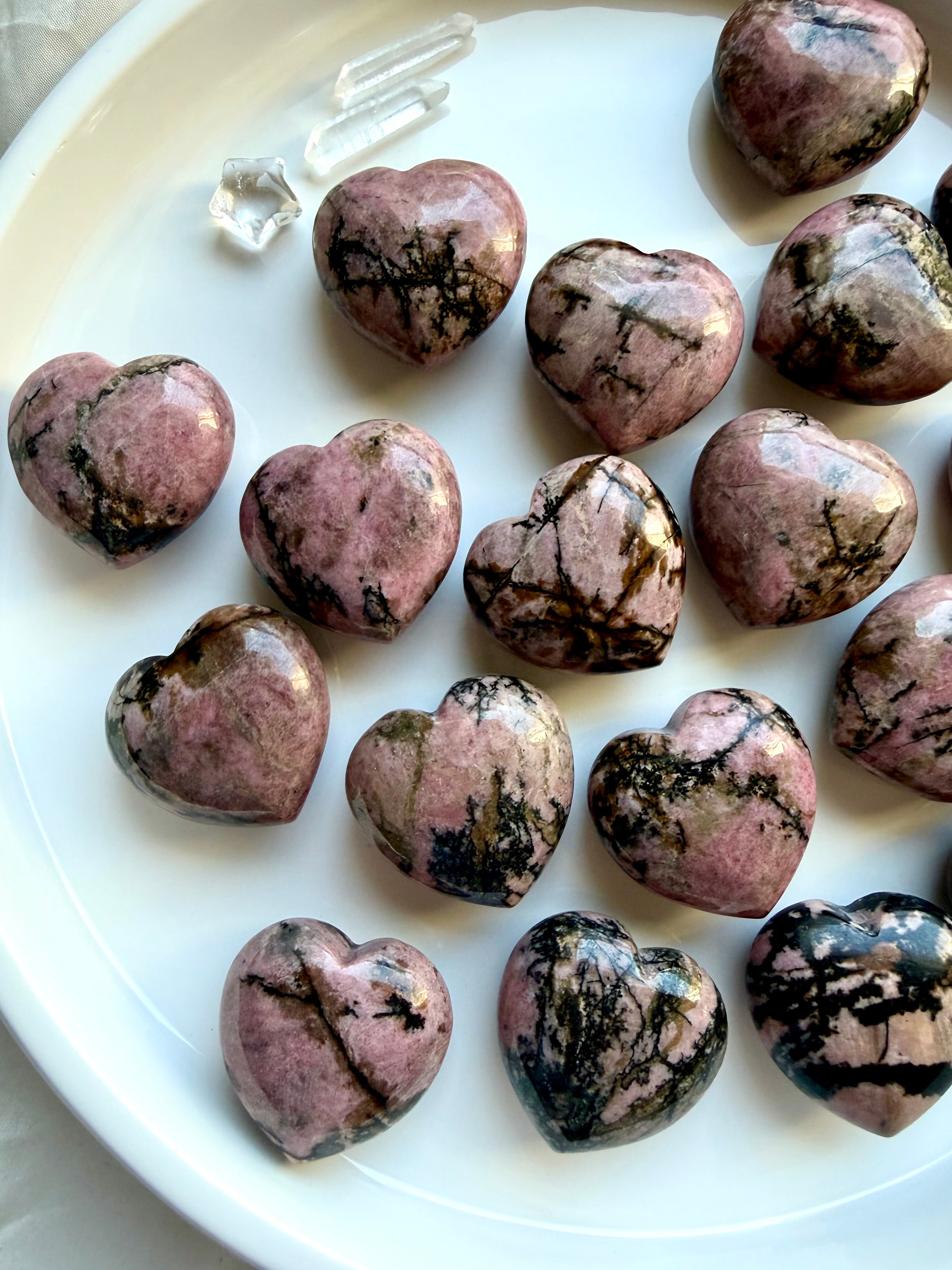 Rhodonite heart stones arranged on a white plate for emotional healing, self-love and Heart Chakra work