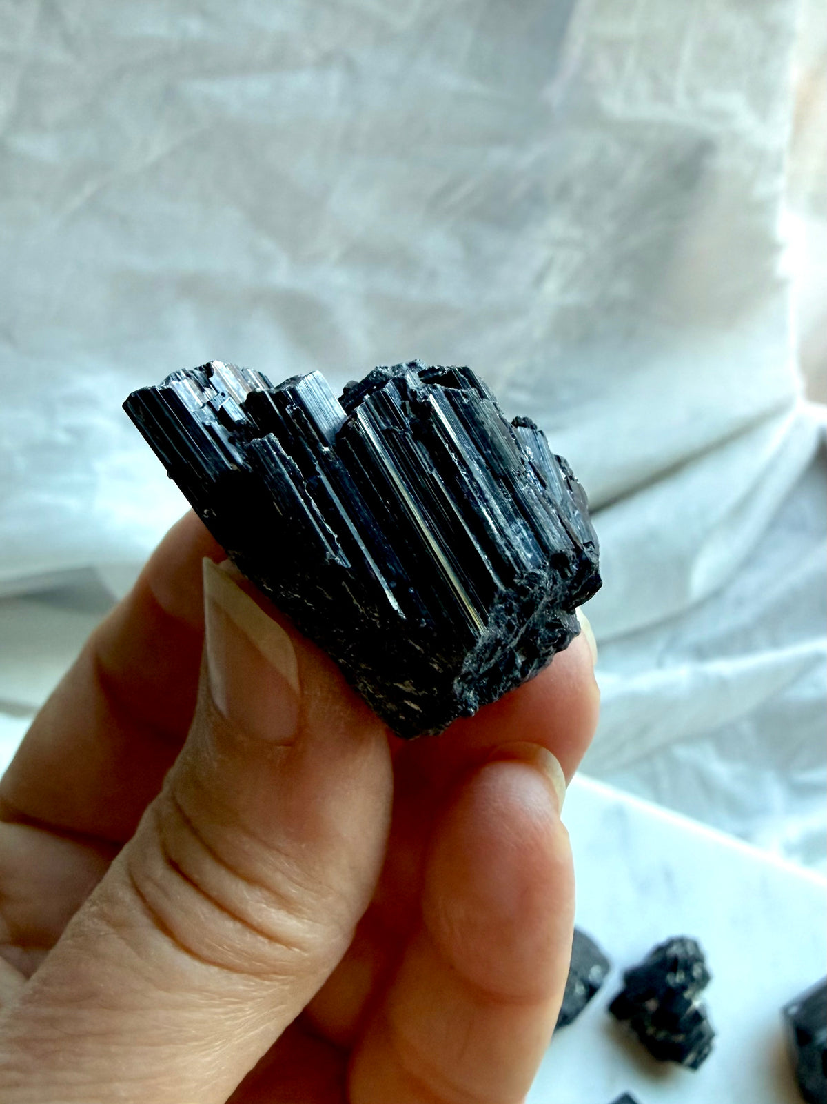 Raw Black Tourmaline chunk held in hand with deep black color and natural columnar crystal formation