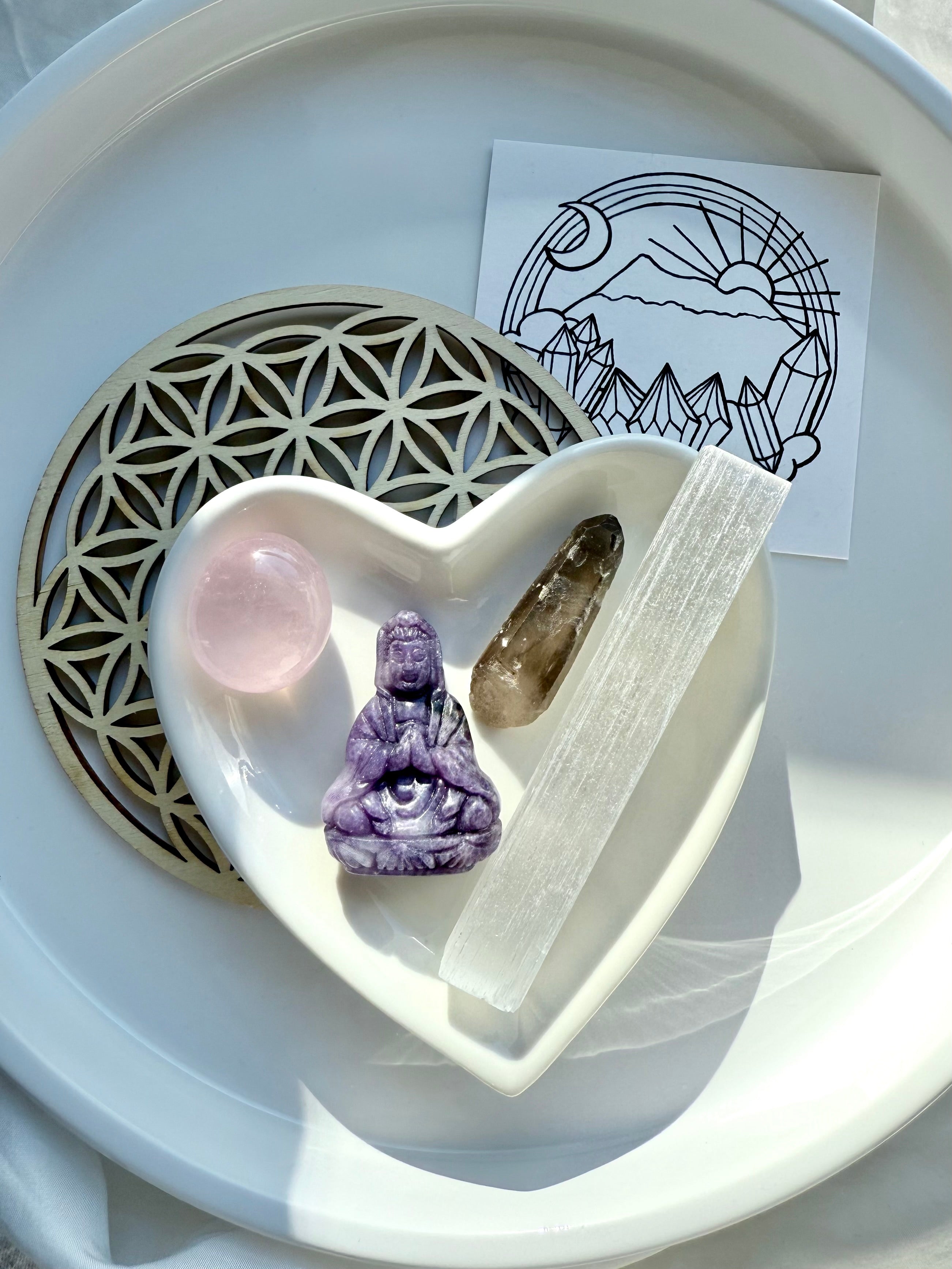 Heart-shaped dish holding goddess crystal set with cosmic altar card and flower of life grid in white tray