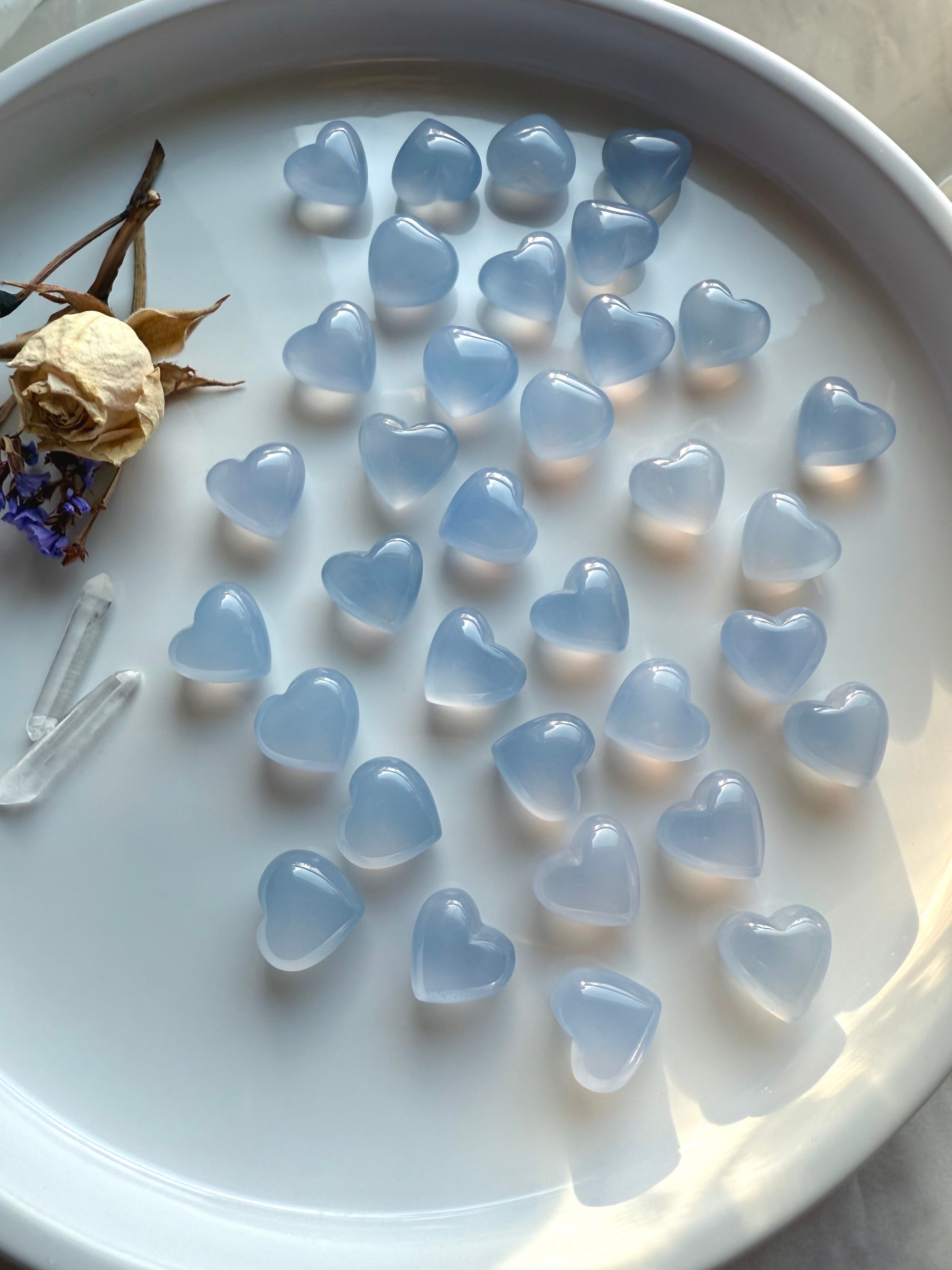 Mini Blue Chalcedony heart crystals arranged on a white tray with clear quartz points and dried flowers, calming Throat Chakra stones for peaceful communication and emotional harmony