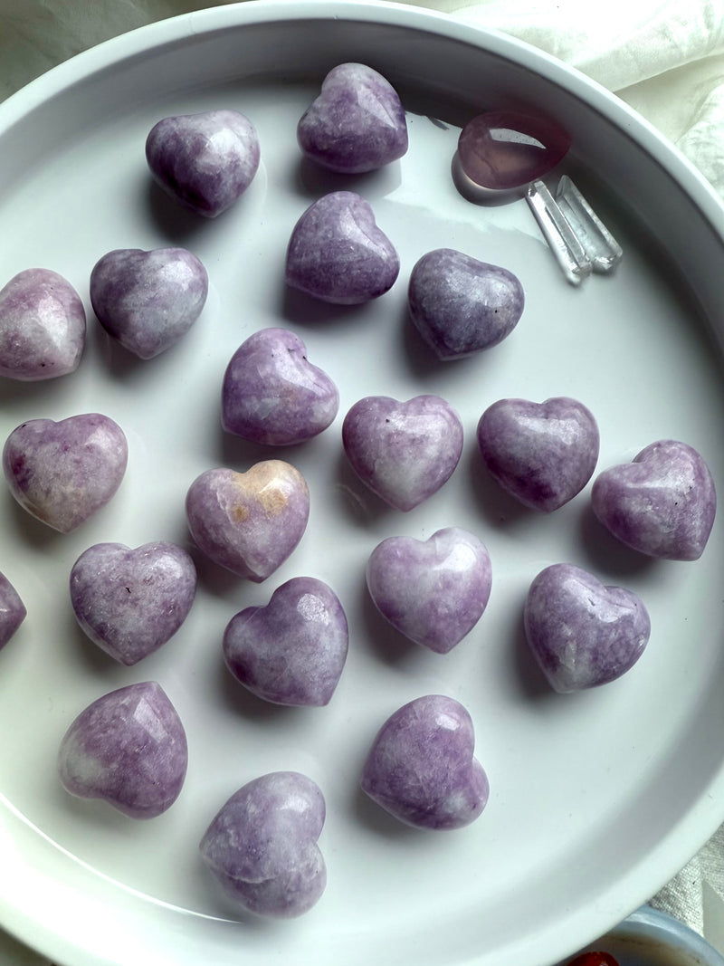 An array of calming lilac colored Lepidolite puffy hearts shown on a white plate