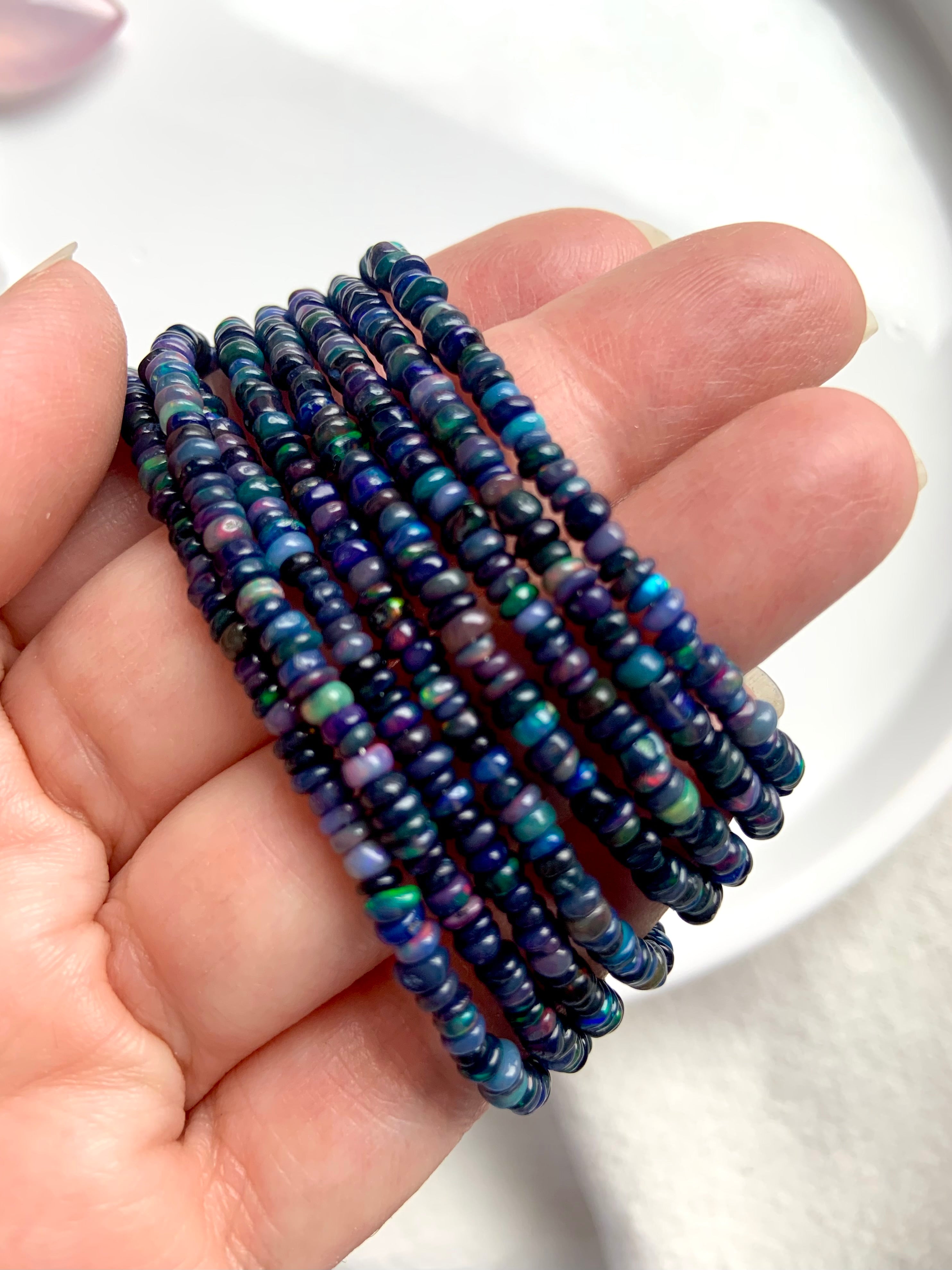 Black Fire Opal bracelets in various bead sizes held at an angle to show blue and rainbow iridescence — sterling silver clasp jewelry.