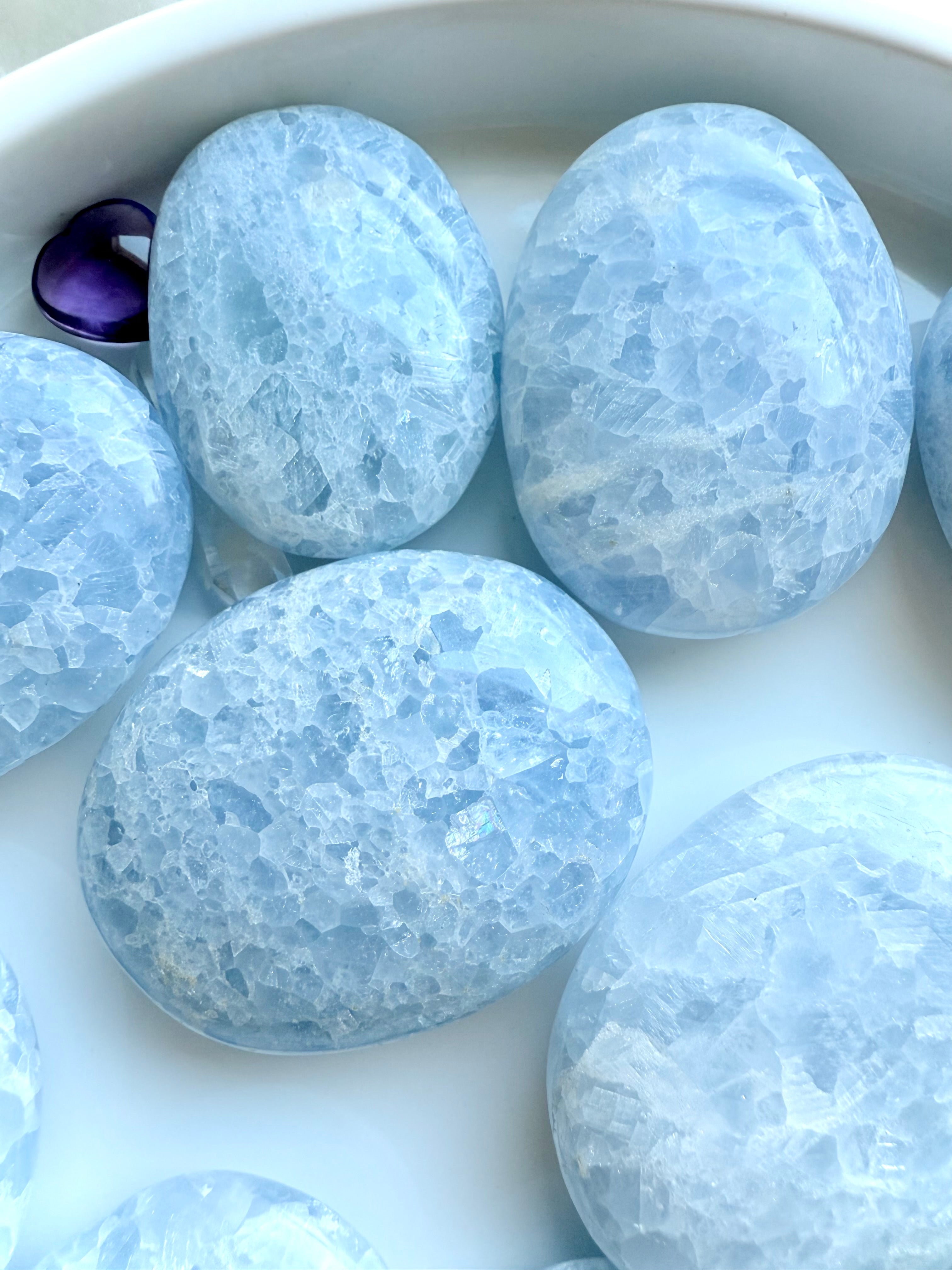 Variety of Blue Calcite palm stones in frosty blue shades, showing size and pattern variations on a white background