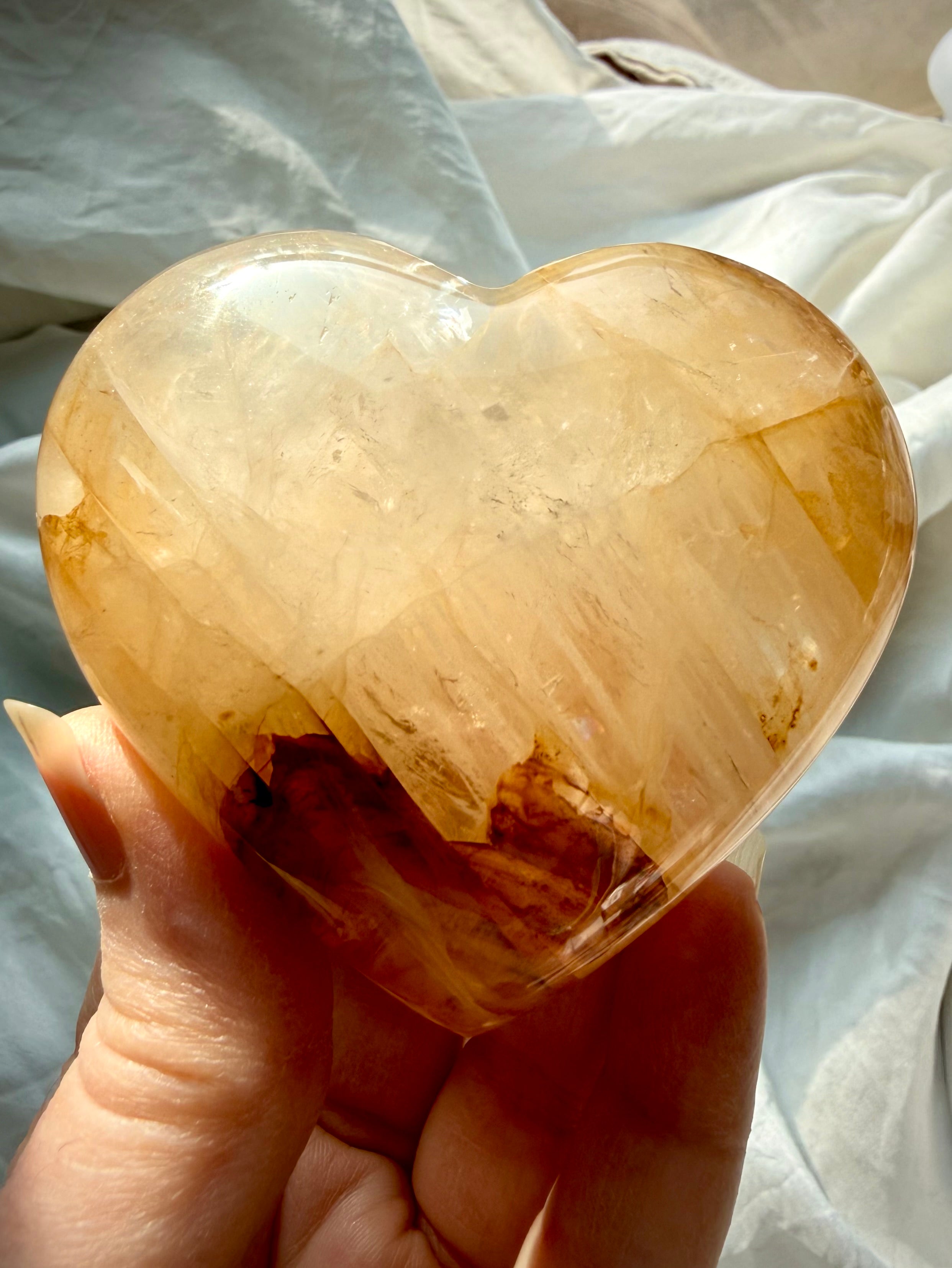 Handheld Golden Healer heart crystal with warm golden tones and natural internal veils for meditation and manifestation