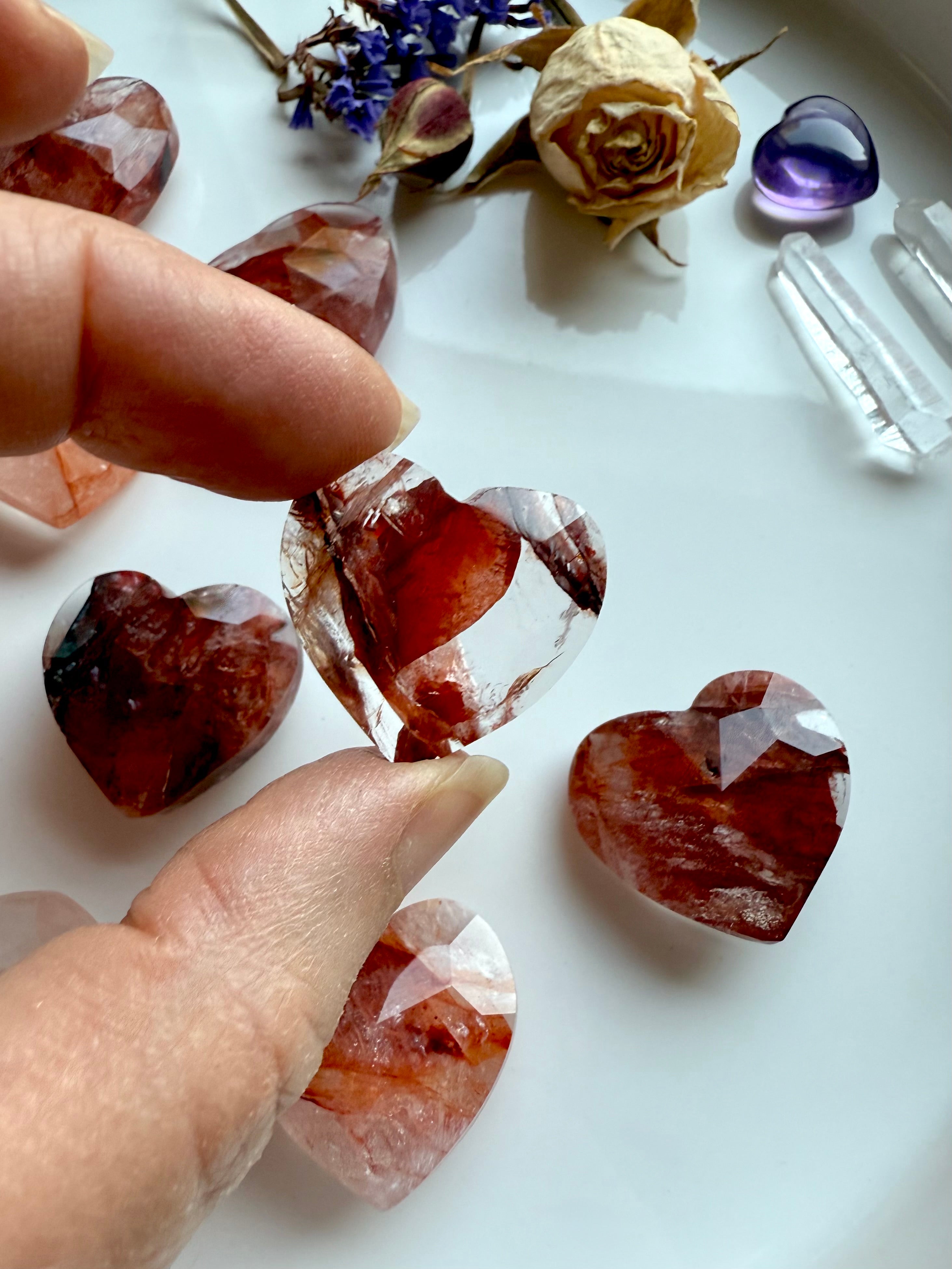 Close-up of faceted Fire Quartz heart crystal with more in the background – mini hematoid quartz hearts for grounding and energy healing