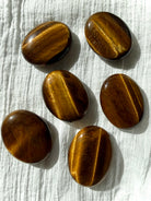 Tiger’s Eye palm stones arranged on white fabric showing beautiful golden flash and earthy brown tones