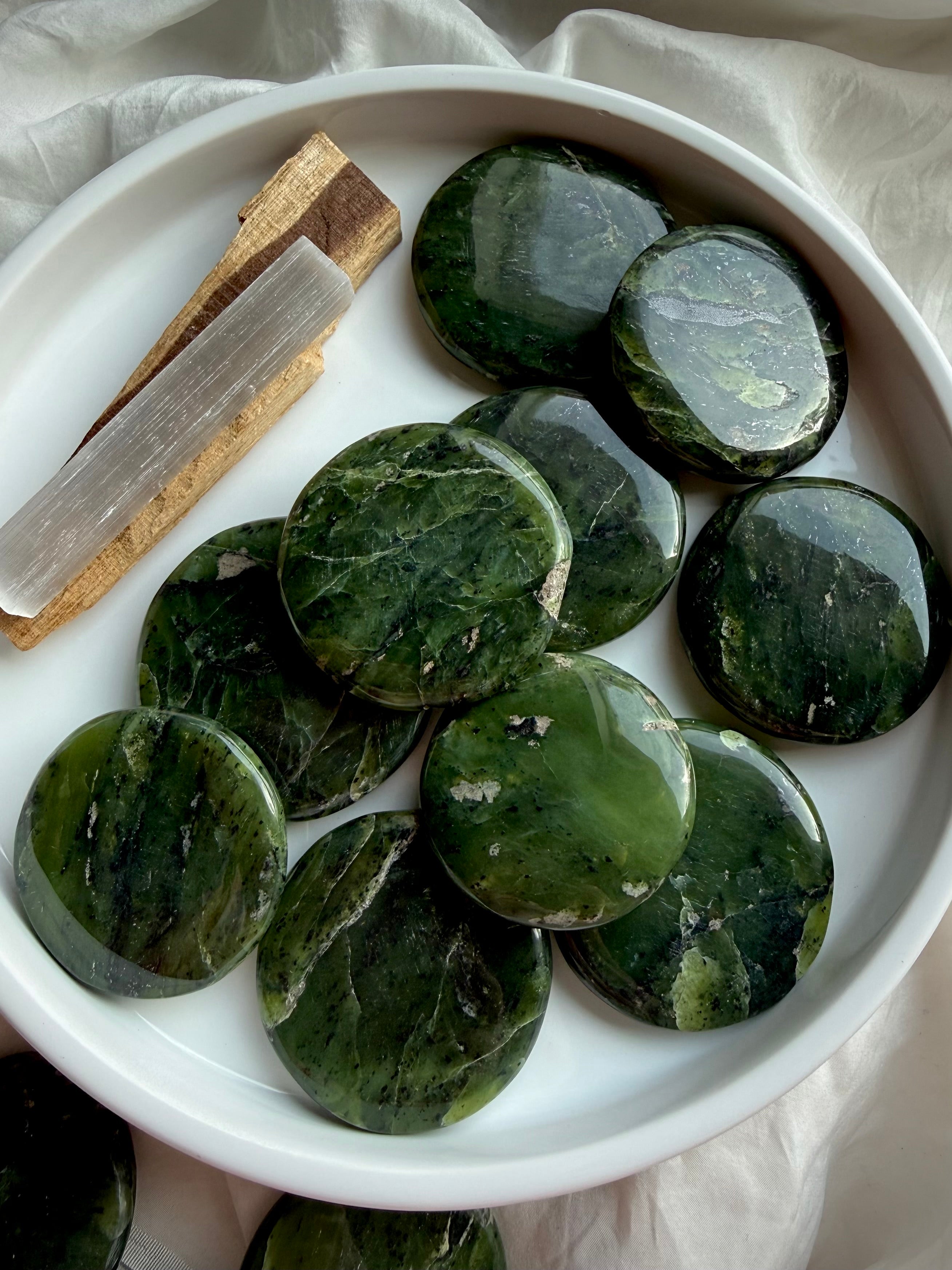 Nephrite jade palm stones in white bowl with selenite stick and palo santo, grounding heart chakra crystals for meditation and emotional balance