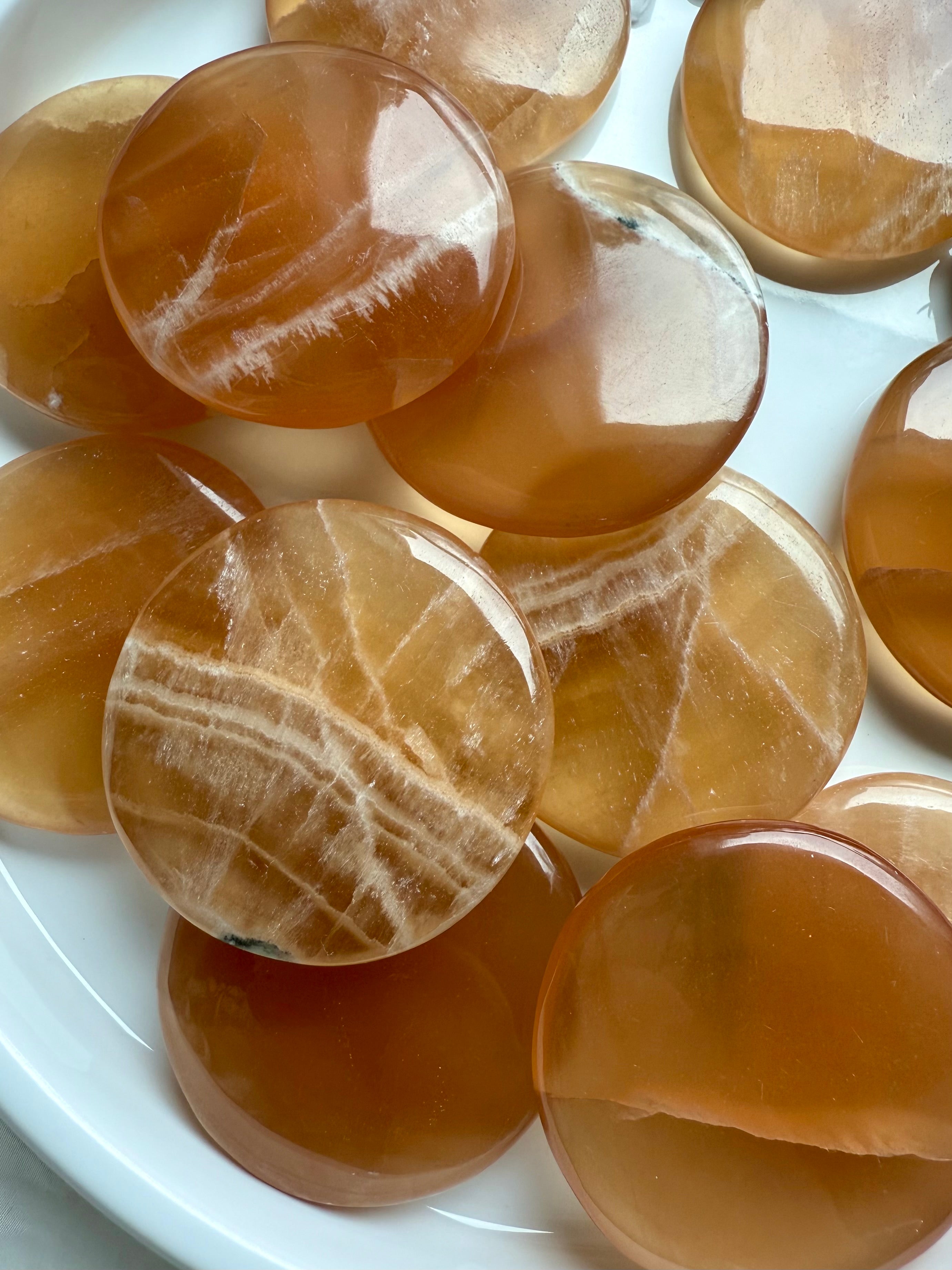 Close-up of polished Honey Calcite palm stones with banded patterns, glowing with warm amber tones for confidence, focus, and gentle empowerment.