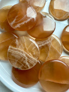 Close-up of polished Honey Calcite palm stones with banded patterns, glowing with warm amber tones for confidence, focus, and gentle empowerment.